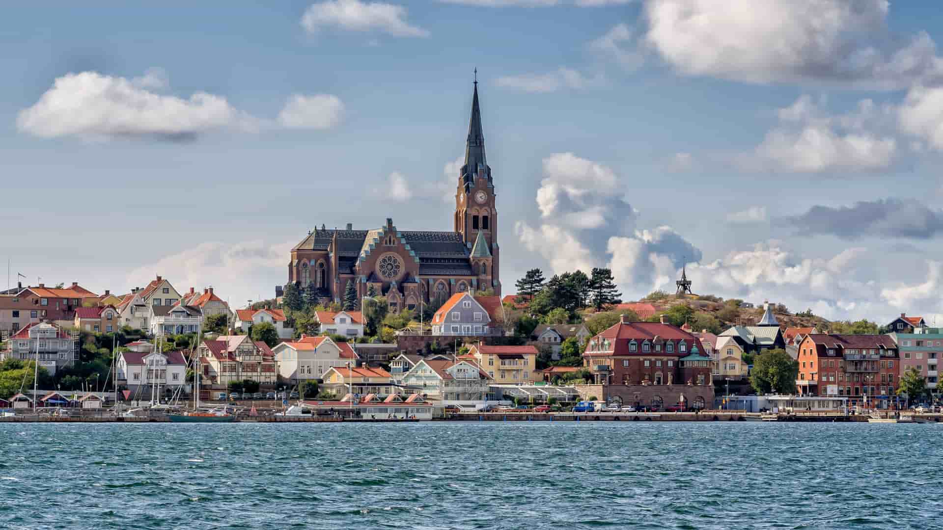 A beautiful image of the coastal town of Lysekil, Sweden, with its colorful houses and a prominent church steeple, seen from the sparkling water of the North Sea.
