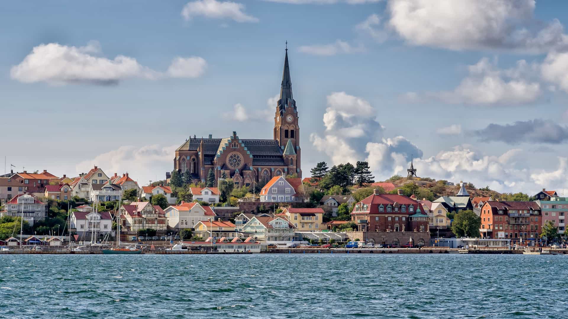 A beautiful image of the coastal town of Lysekil, Sweden, with its colorful houses and a prominent church steeple, seen from the sparkling water of the North Sea.