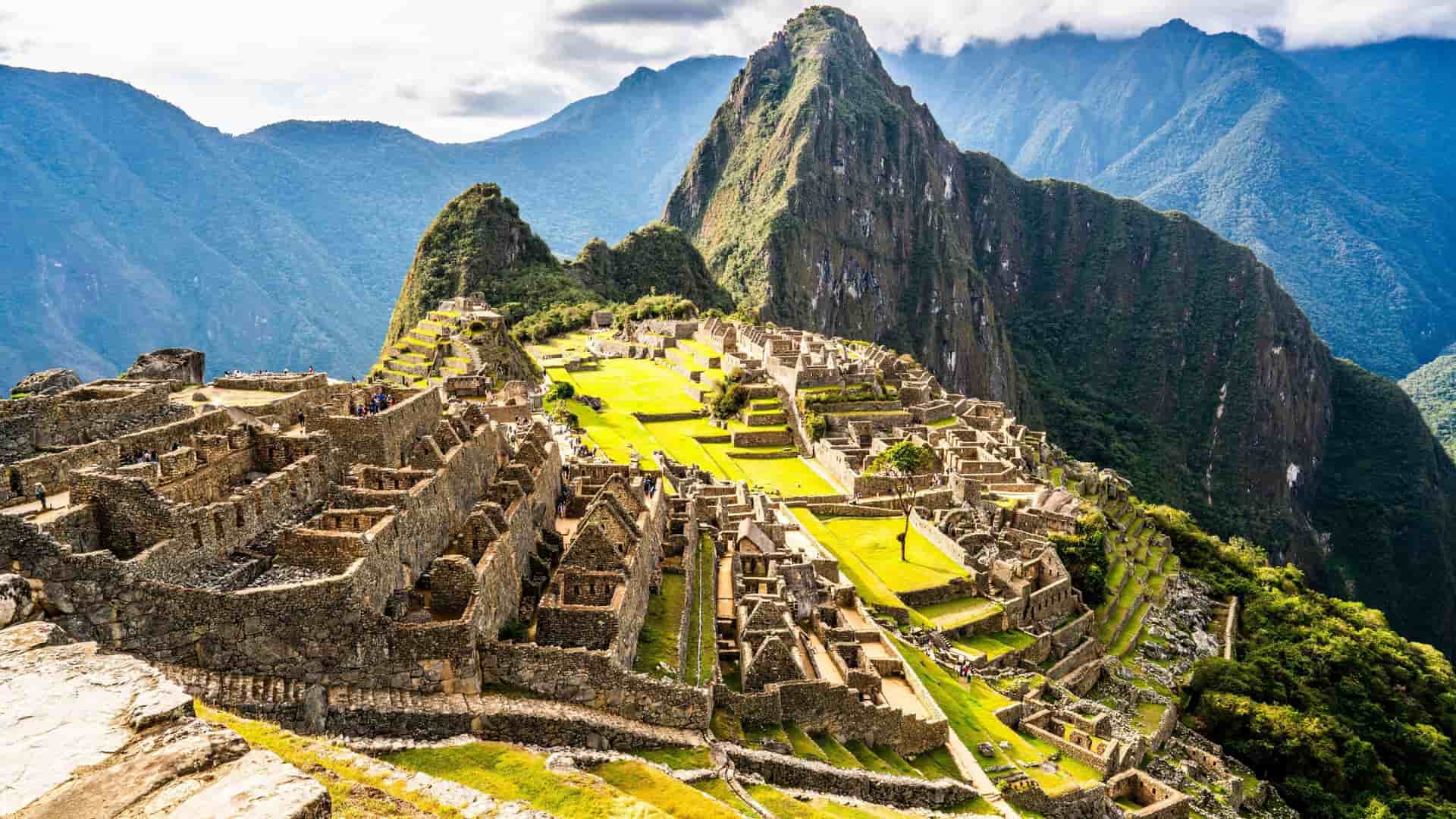 A panoramic view of the ancient Incan citadel of Machu Picchu, a UNESCO World Heritage Site, with its stone terraces and structures surrounded by towering Andes mountains and dramatic valleys.