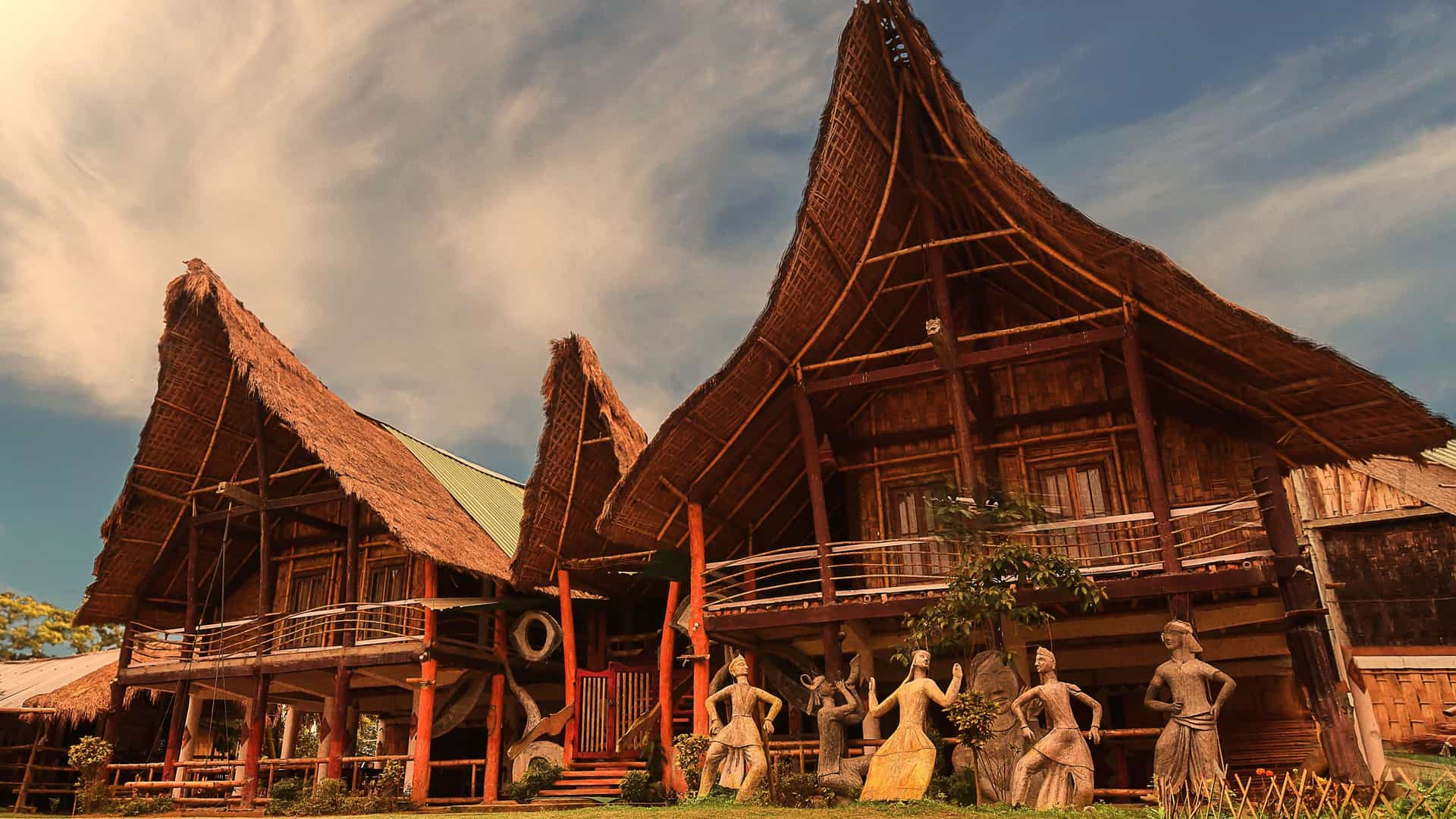 "A wide-angle, low-angle shot of traditional bamboo stilt houses with thatched roofs in a village on Majuli Island, India, under a dramatic cloudy sky. "