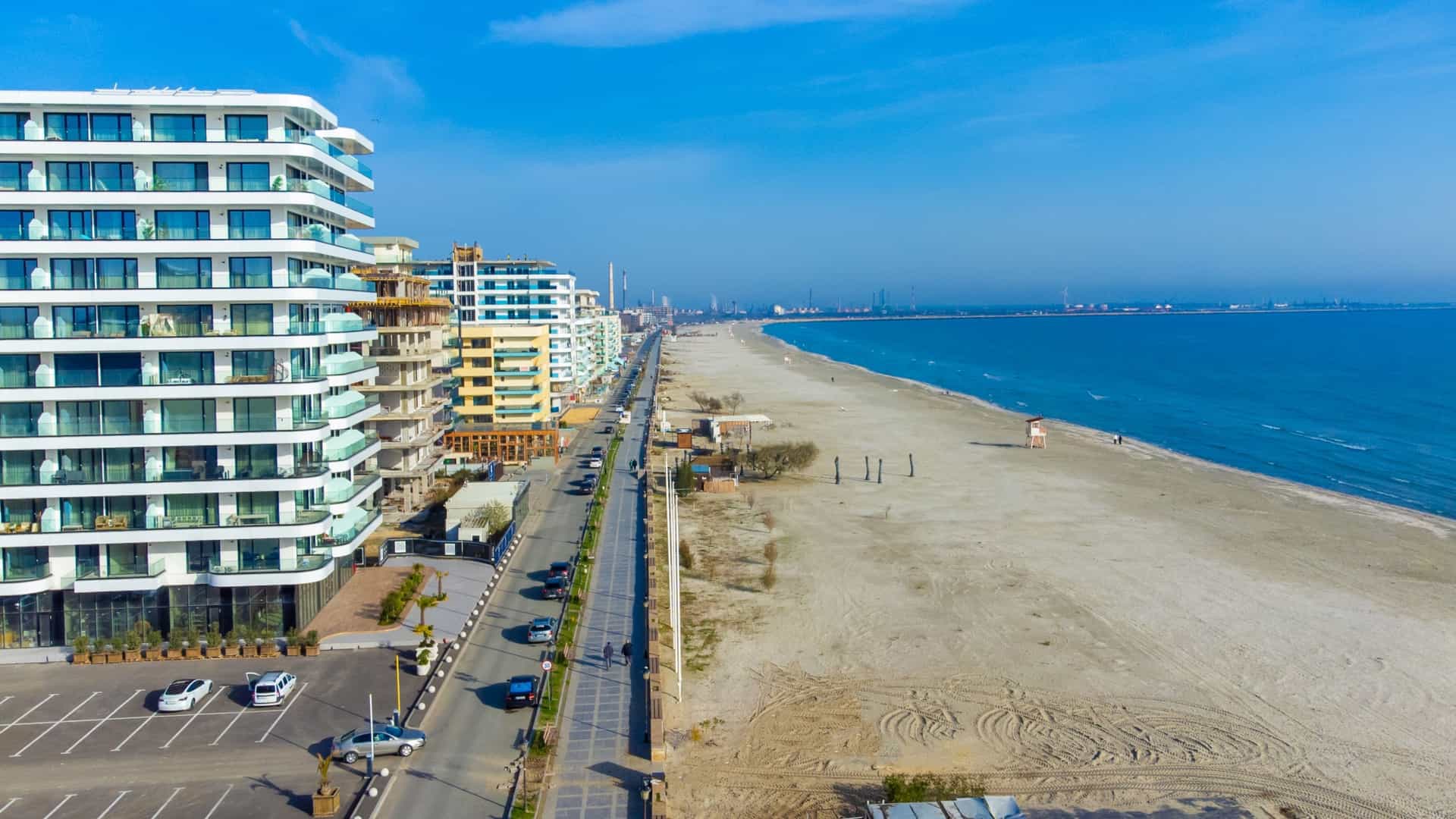Modern, white high-rise apartments line the long, wide sandy beach and calm blue water in the resort of Mamaia, Romania.