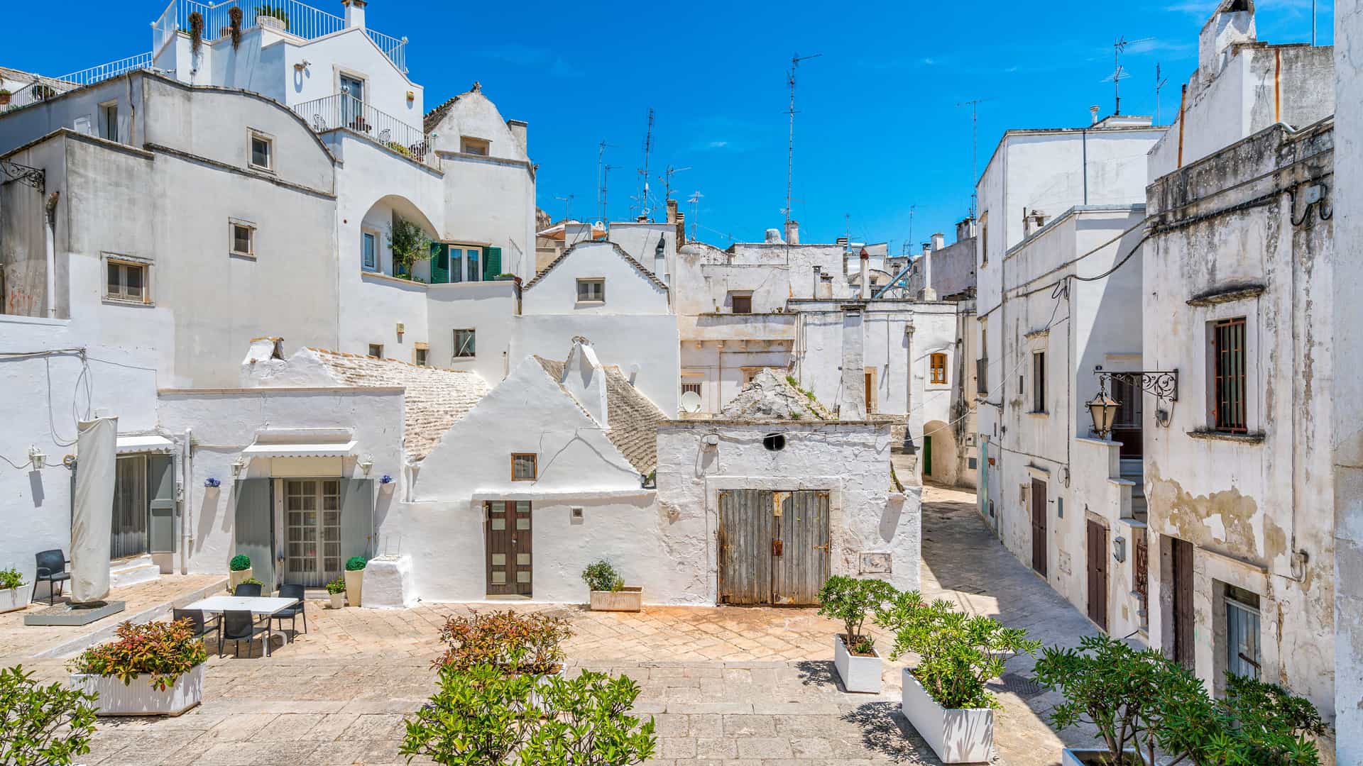 "A sunlit narrow courtyard in the historic center of Martina Franca, Italy, with traditional whitewashed buildings and charming cobblestone streets. "