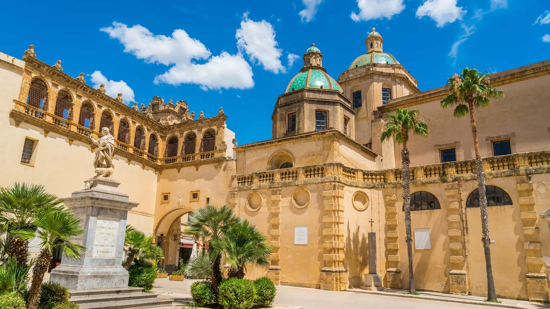 "A vibrant street view of the historic Piazza della Repubblica in Mazara del Vallo, Italy, showcasing the baroque Church of San Vito in Mazara and the seminary building under a bright blue sky. "