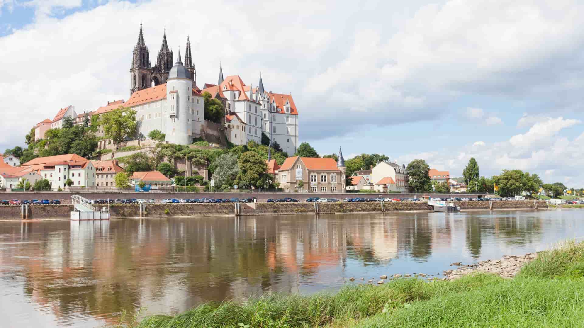 A wide-angle view of the historic Albrechtsburg Castle and the Meissen Cathedral, located on a hill overlooking the Elbe River in Meissen, Germany.