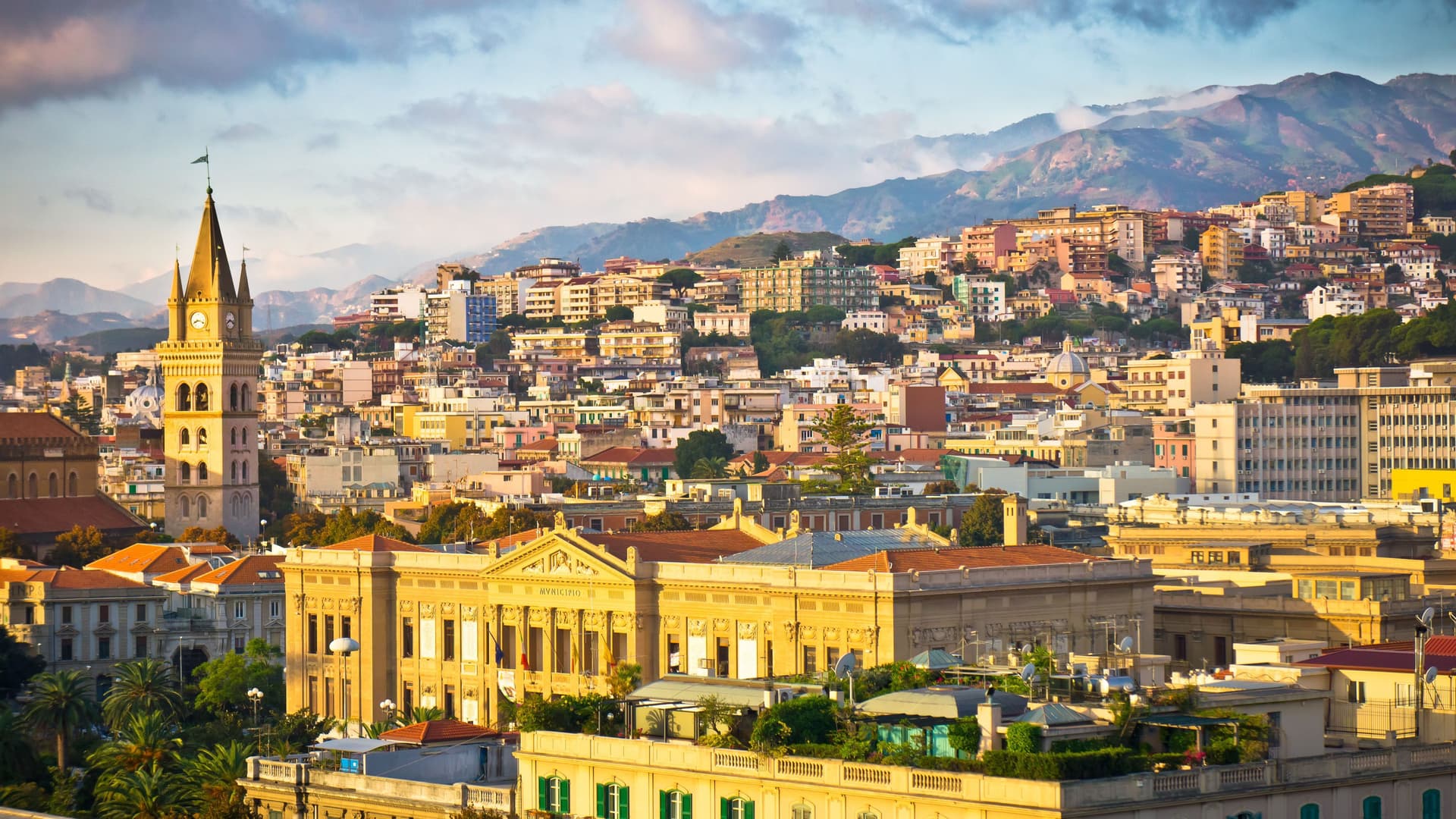 A vibrant panoramic view of the bustling city of Messina, Sicily, with its colorful buildings and a prominent clock tower nestled at the base of lush green mountains.