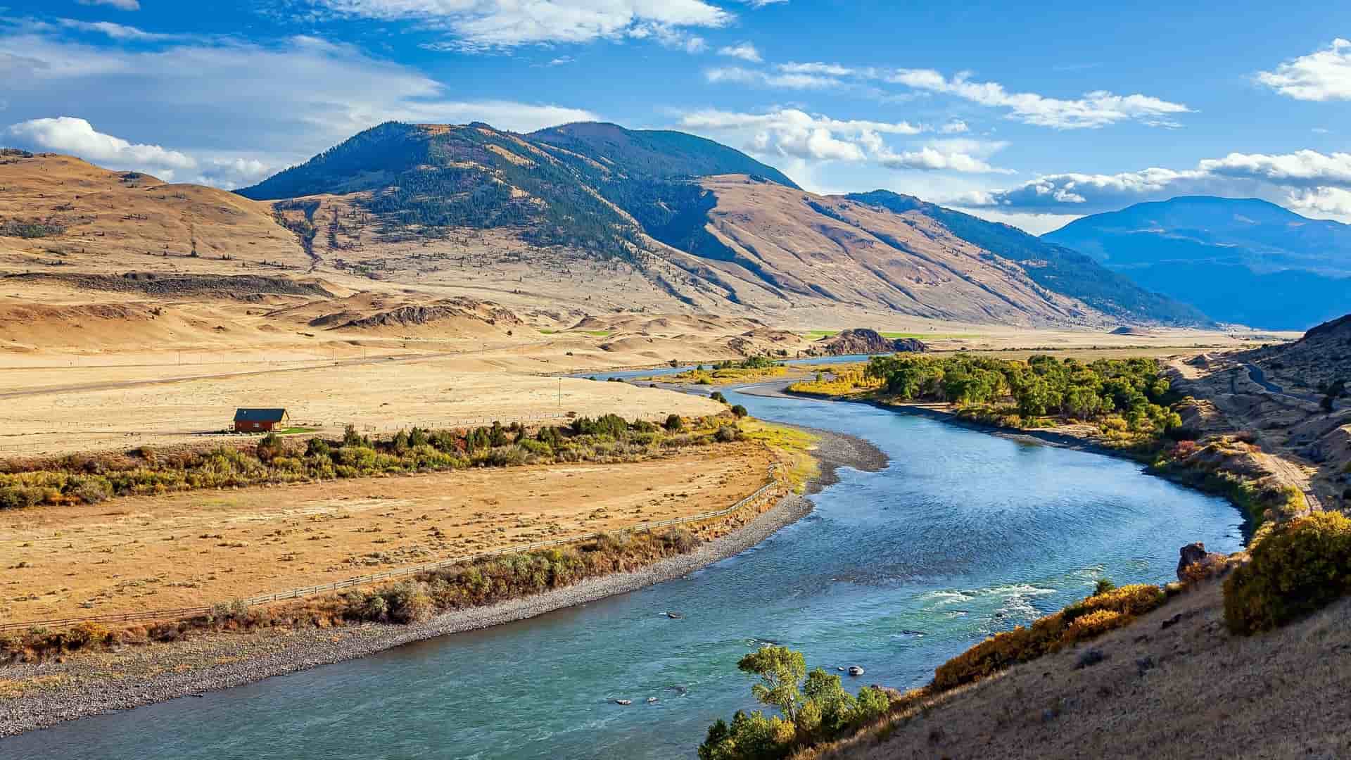 A beautiful and wide scenic view of the Mississippi River winding through a vast valley, surrounded by majestic mountains and rugged landscapes under a bright blue sky.