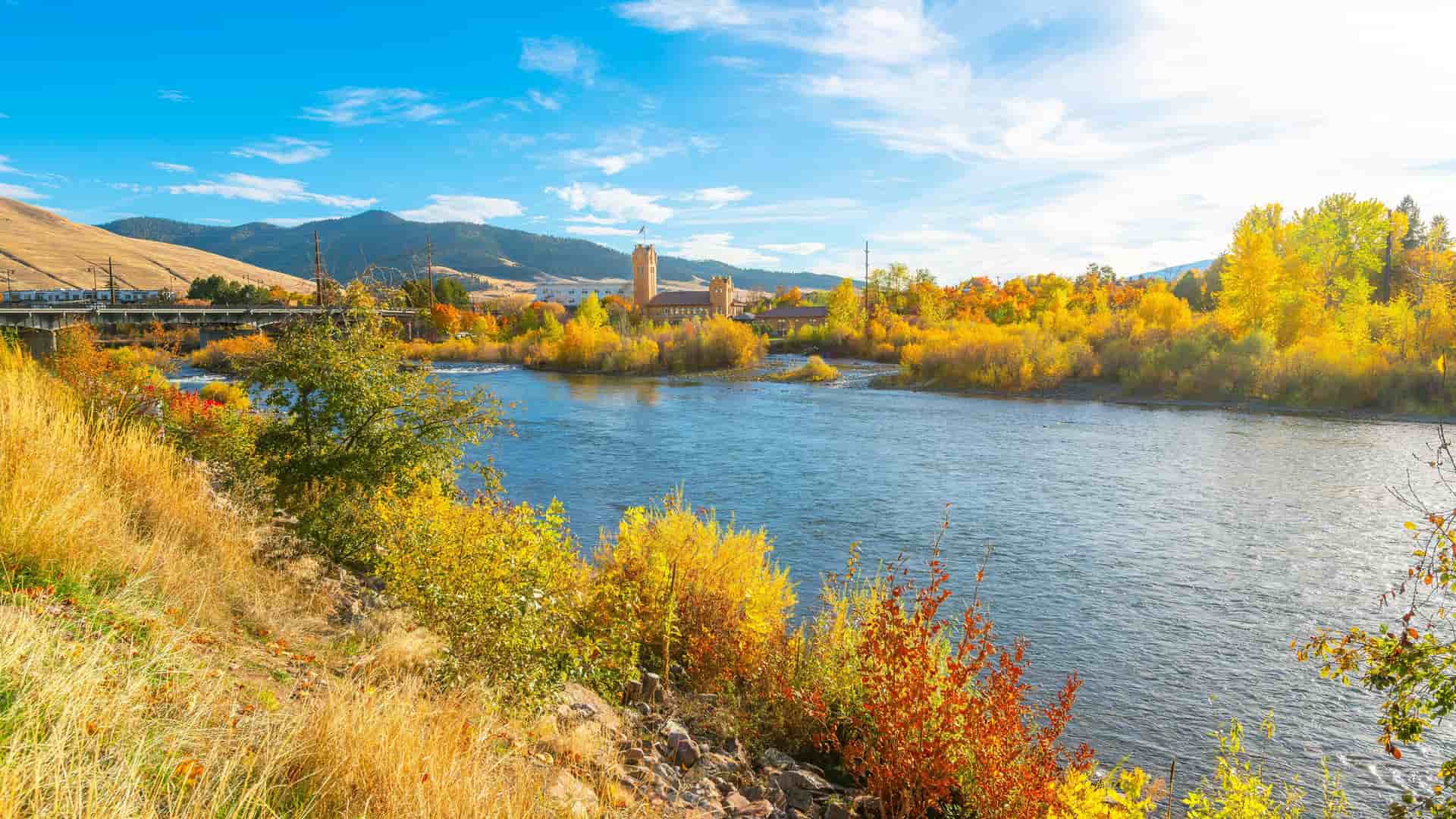"A stunning autumn view of the Clark Fork River in Missoula, Montana, with the historic Milwaukee Depot in the background and vibrant yellow foliage along the riverbank. "