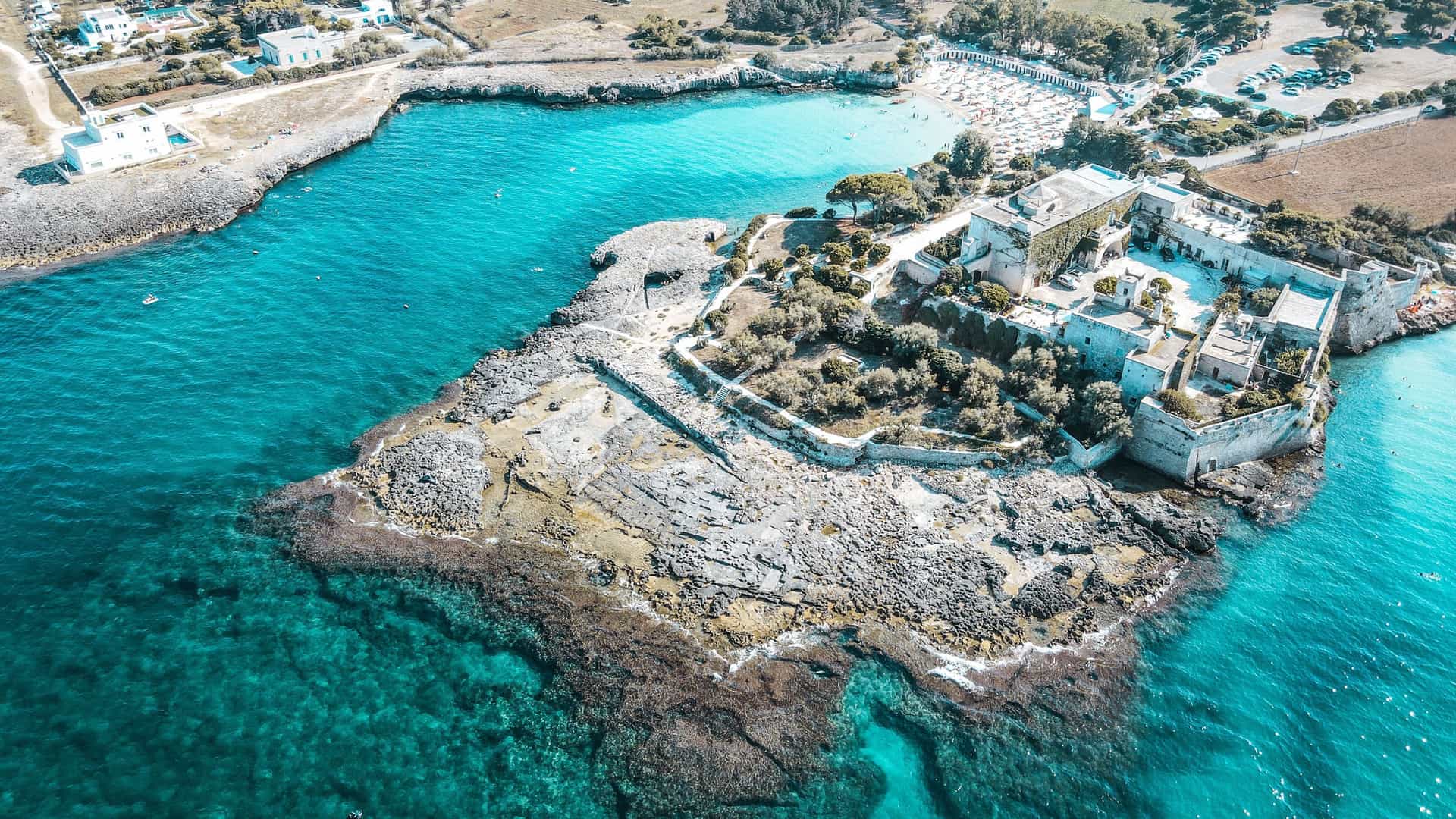 An aerial view of an ancient fortress and castle, the Castello di Santo Stefano, situated on a rocky peninsula surrounded by the clear turquoise waters of the Adriatic Sea near Monopoli, Italy.