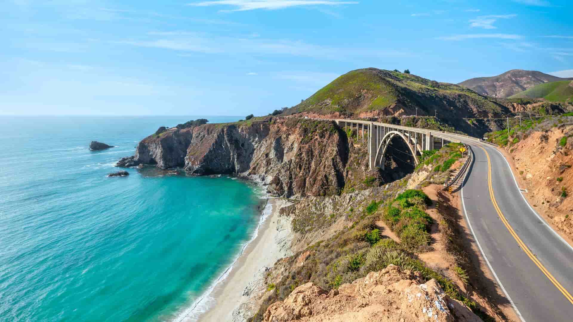 "A high-angle scenic view of the iconic Bixby Bridge in Monterey, California, spanning a coastal gorge along the beautiful Pacific Coast Highway. "