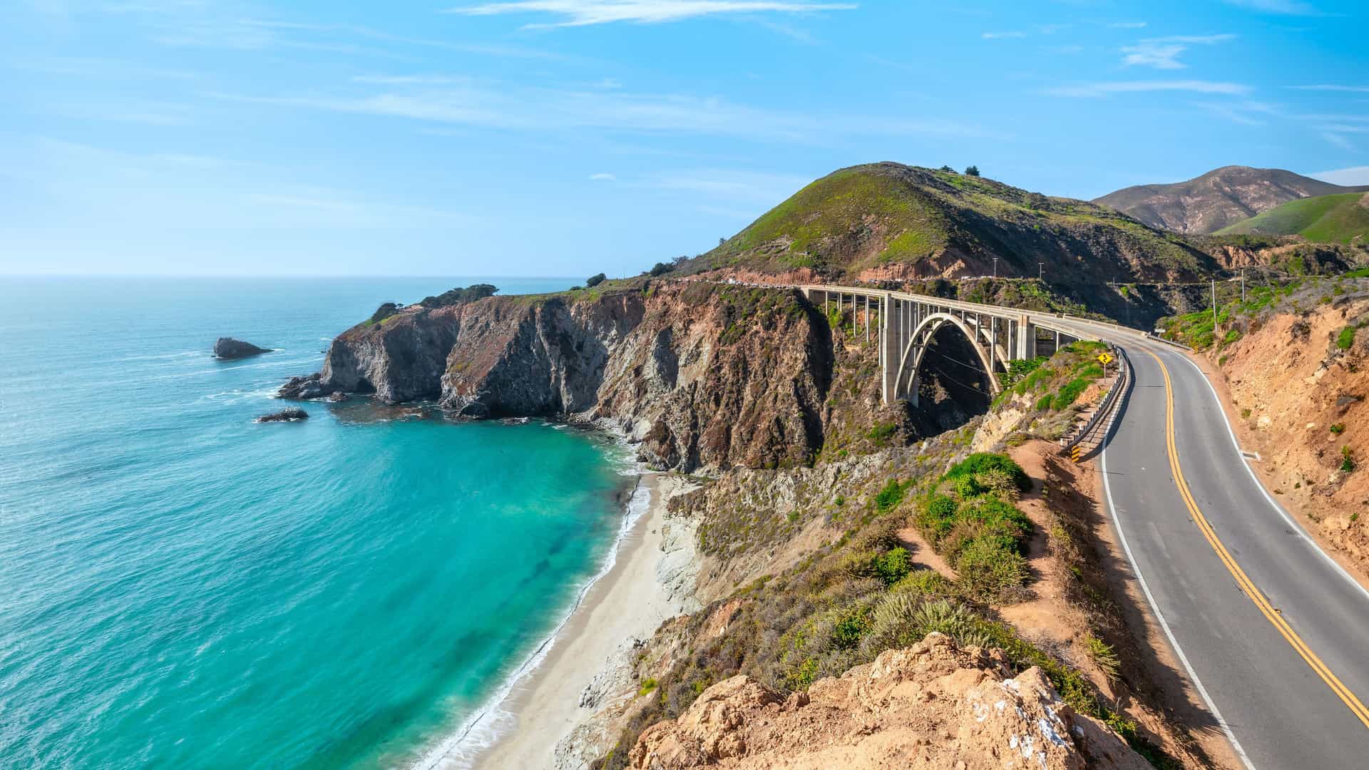 "A high-angle scenic view of the iconic Bixby Bridge in Monterey, California, spanning a coastal gorge along the beautiful Pacific Coast Highway. "