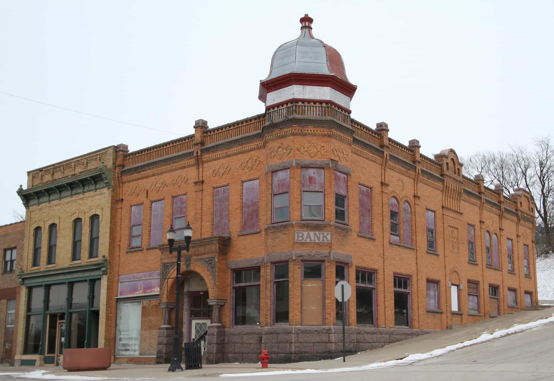 A weathered, historic, red brick building in Montevideo, Minnesota, with a distinctive turret and boarded-up windows, located on a street corner with snow on the ground.