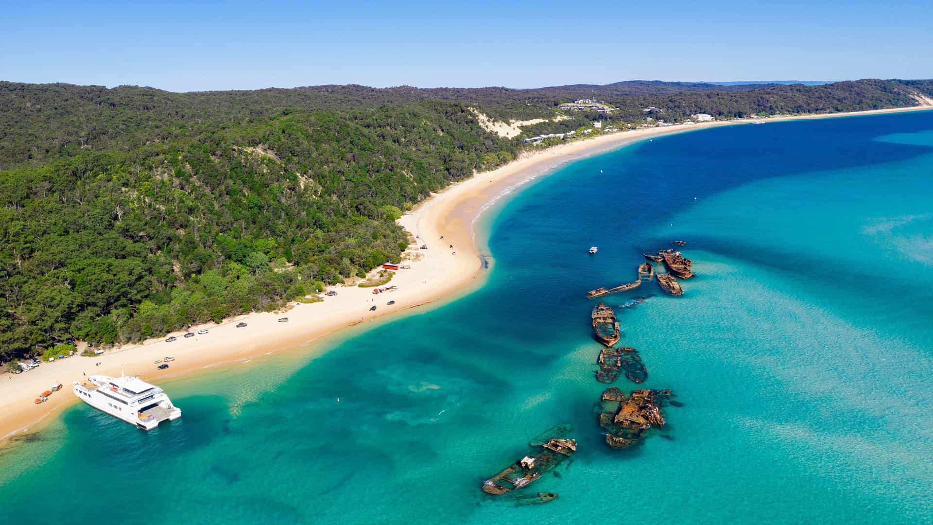 An aerial view of Moreton Island, Australia, showcasing the iconic Tangalooma Wrecks, a series of sunken ships creating an artificial reef off the beautiful white sandy beach.