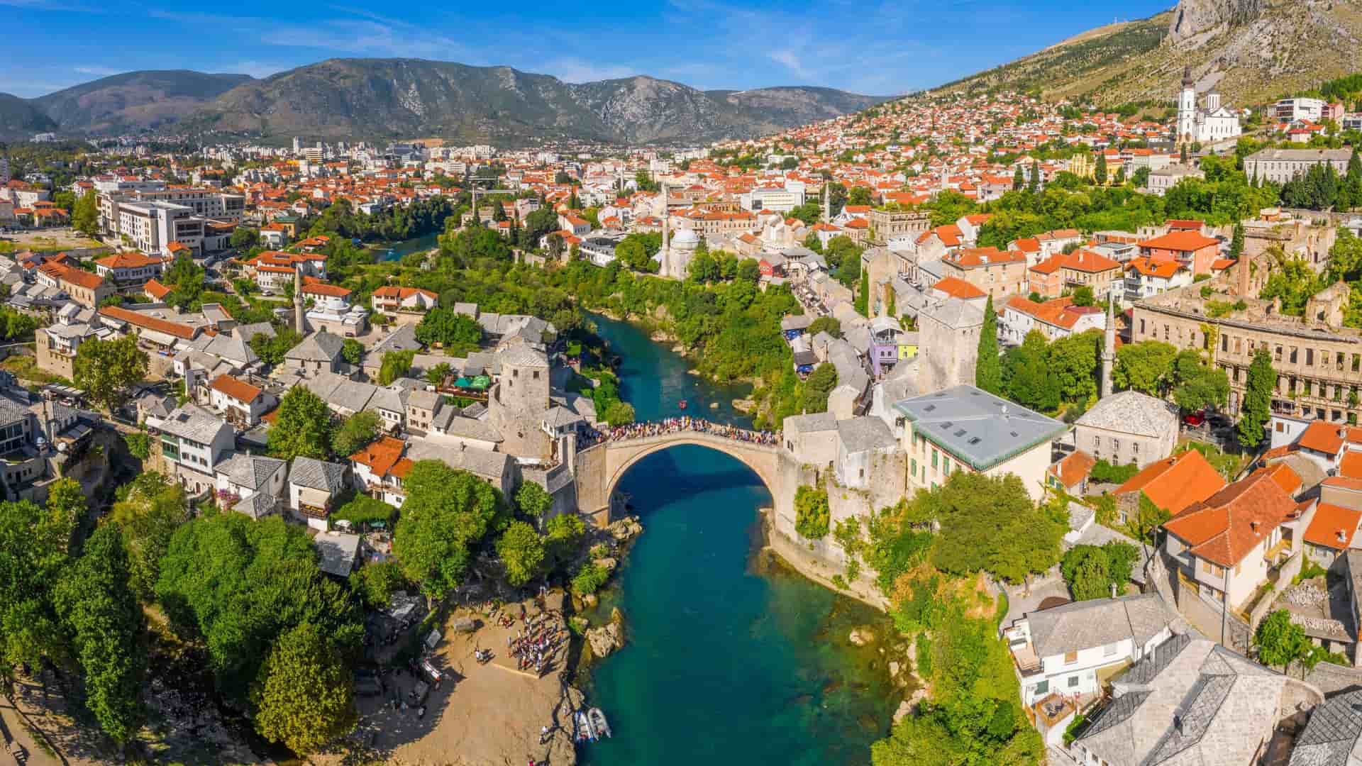 An aerial view of the historic Stari Most bridge in Mostar, Bosnia and Herzegovina, gracefully arching over the turquoise Neretva River and surrounded by the city's traditional Ottoman-era architecture.