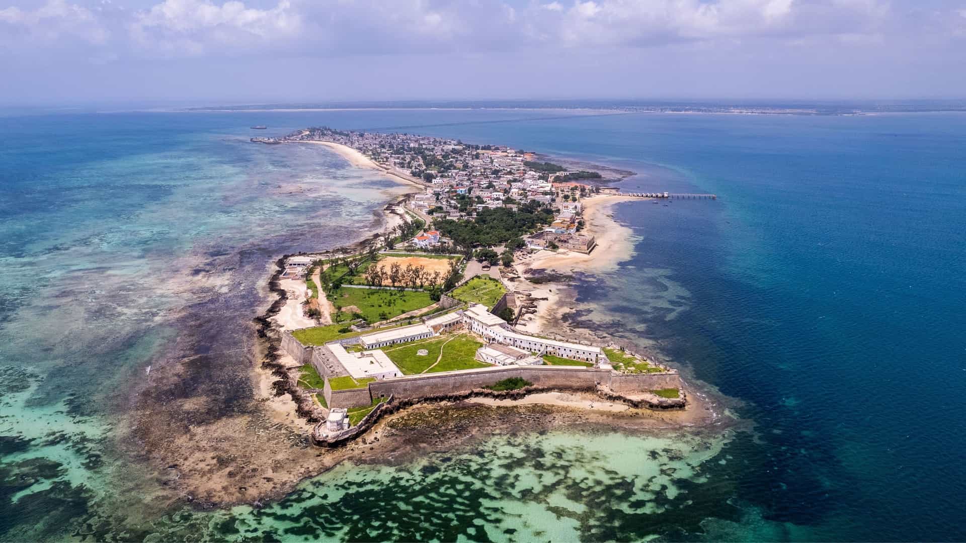 An aerial view of a Portuguese fort on the Ilha de Mozambique in the Mozambique Channel, with turquoise waters and the historic town behind it.