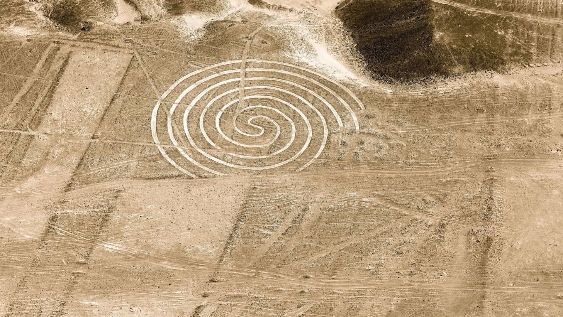 An aerial sepia-toned shot of the Nazca Lines in Peru, showing the intricate geoglyph of a spiral carved into the vast, dry desert landscape.