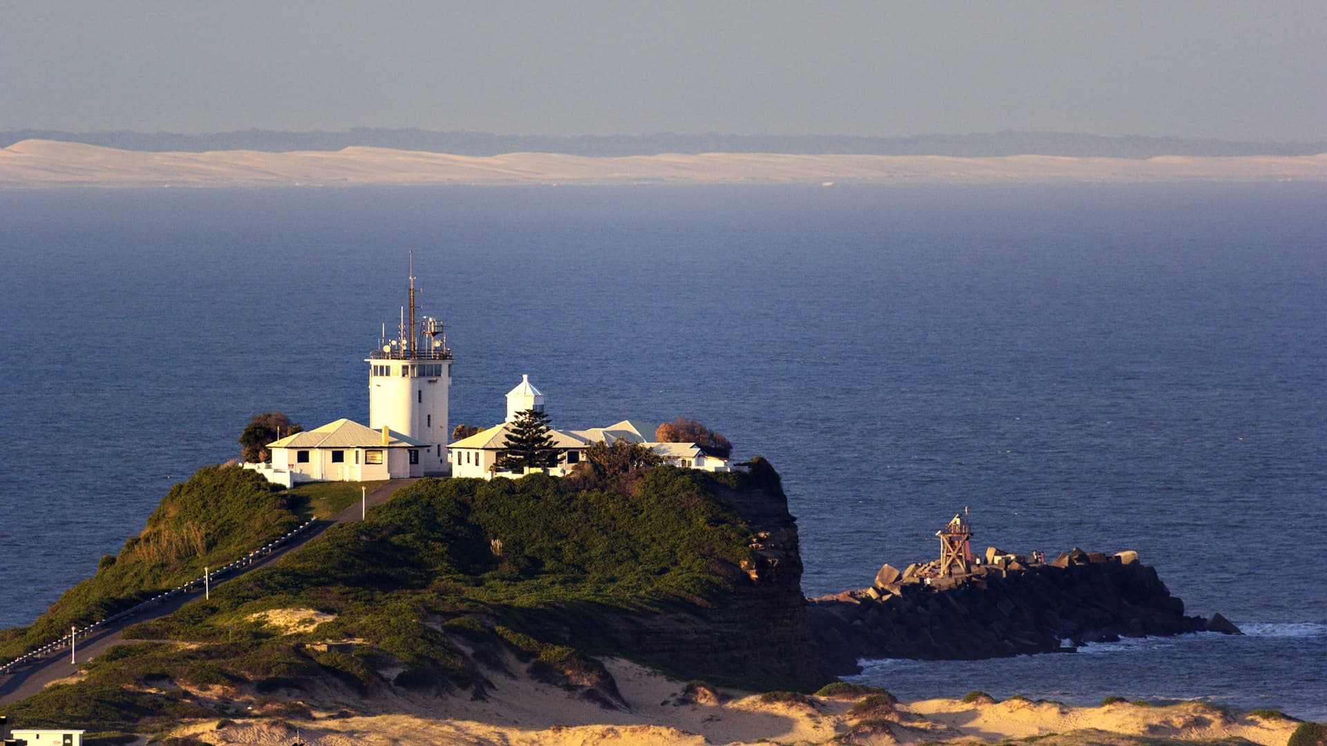 A stunning view of Nobbys Head Lighthouse and Signal Station in Newcastle, NSW, Australia, perched on a headland overlooking the deep blue Pacific Ocean.