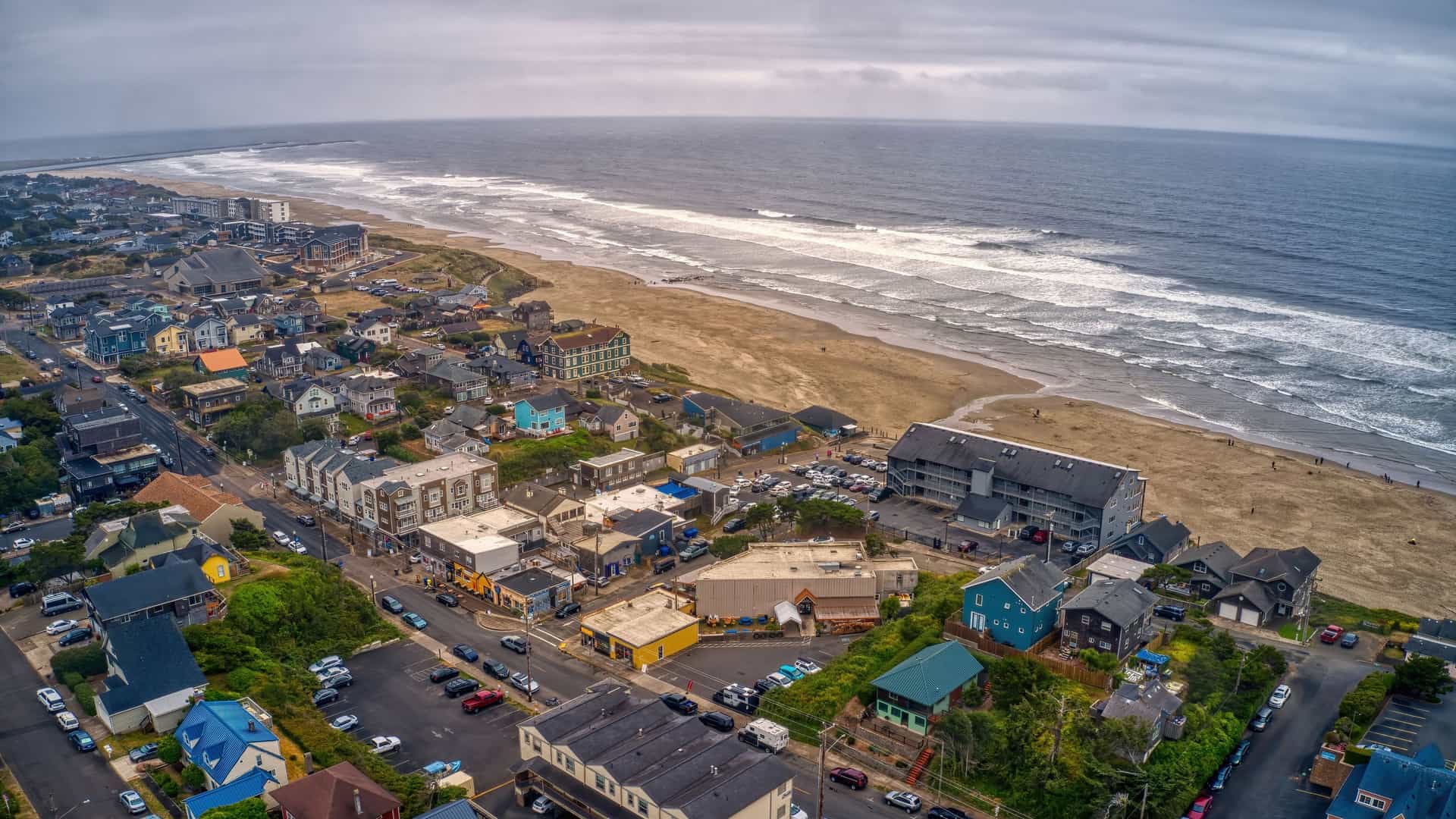 "An aerial view of the scenic coastline of Newport, Oregon, showing the beachfront hotels, houses, and the sandy beach stretching along the Pacific Ocean. "