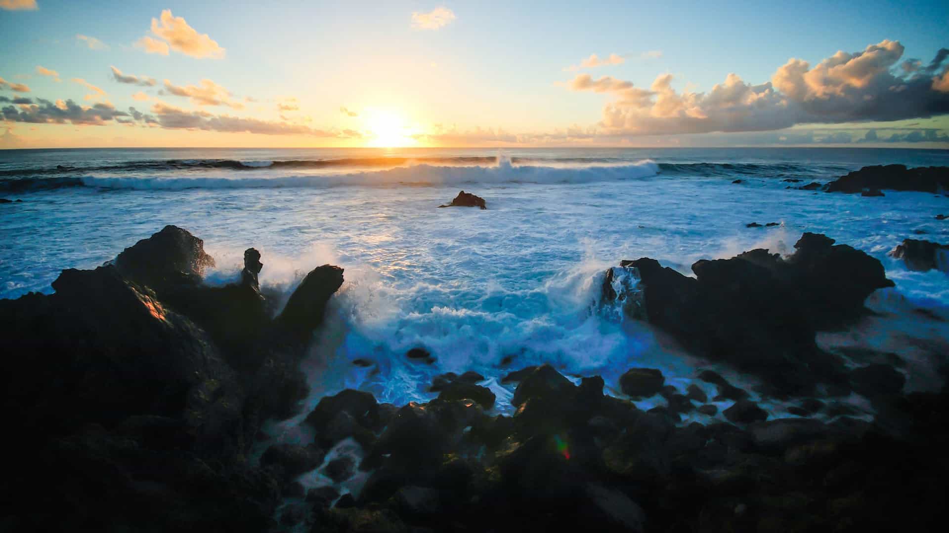 A dramatic sunset view over a rocky coastline with waves crashing against the rocks in Niebla, Chile.