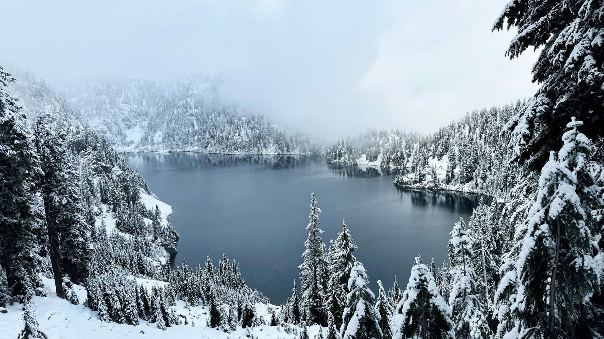 "A stunning panoramic shot of a serene winter landscape at Snow Lake, a popular hiking trail near North Bend, Washington, covered in fresh snow. "