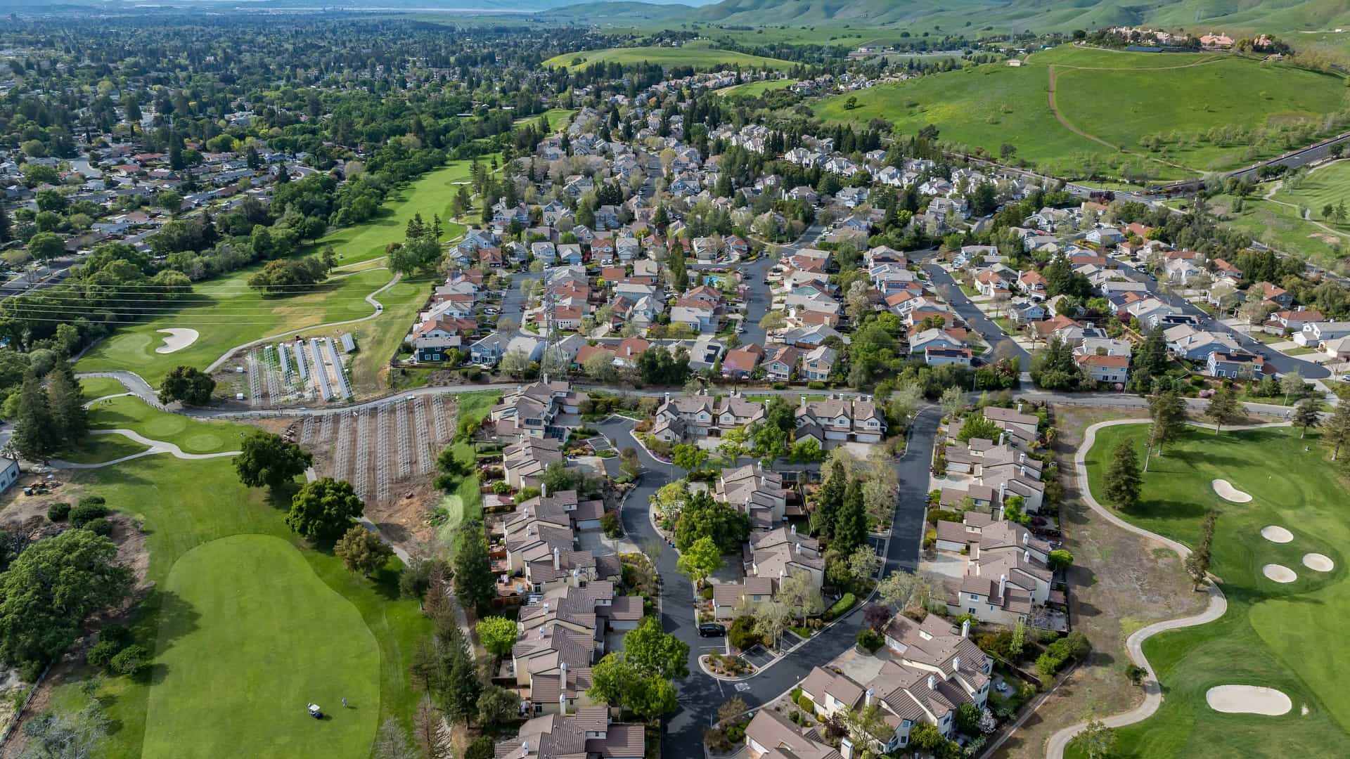 "An aerial view of the suburban community of Oakhurst, California, surrounded by green hills, residential houses, and golf courses on a beautiful sunny day. "