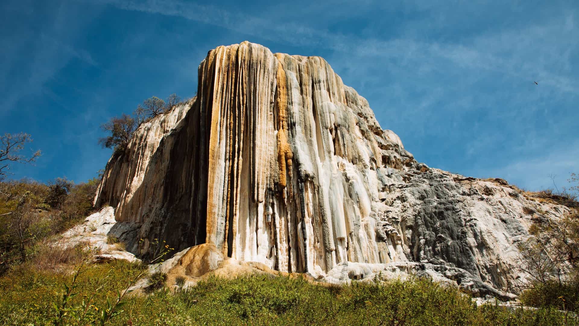 A giant petrified waterfall, Hierve el Agua, in Oaxaca, Mexico, shows vertical mineral deposits in shades of white, orange, and gray.