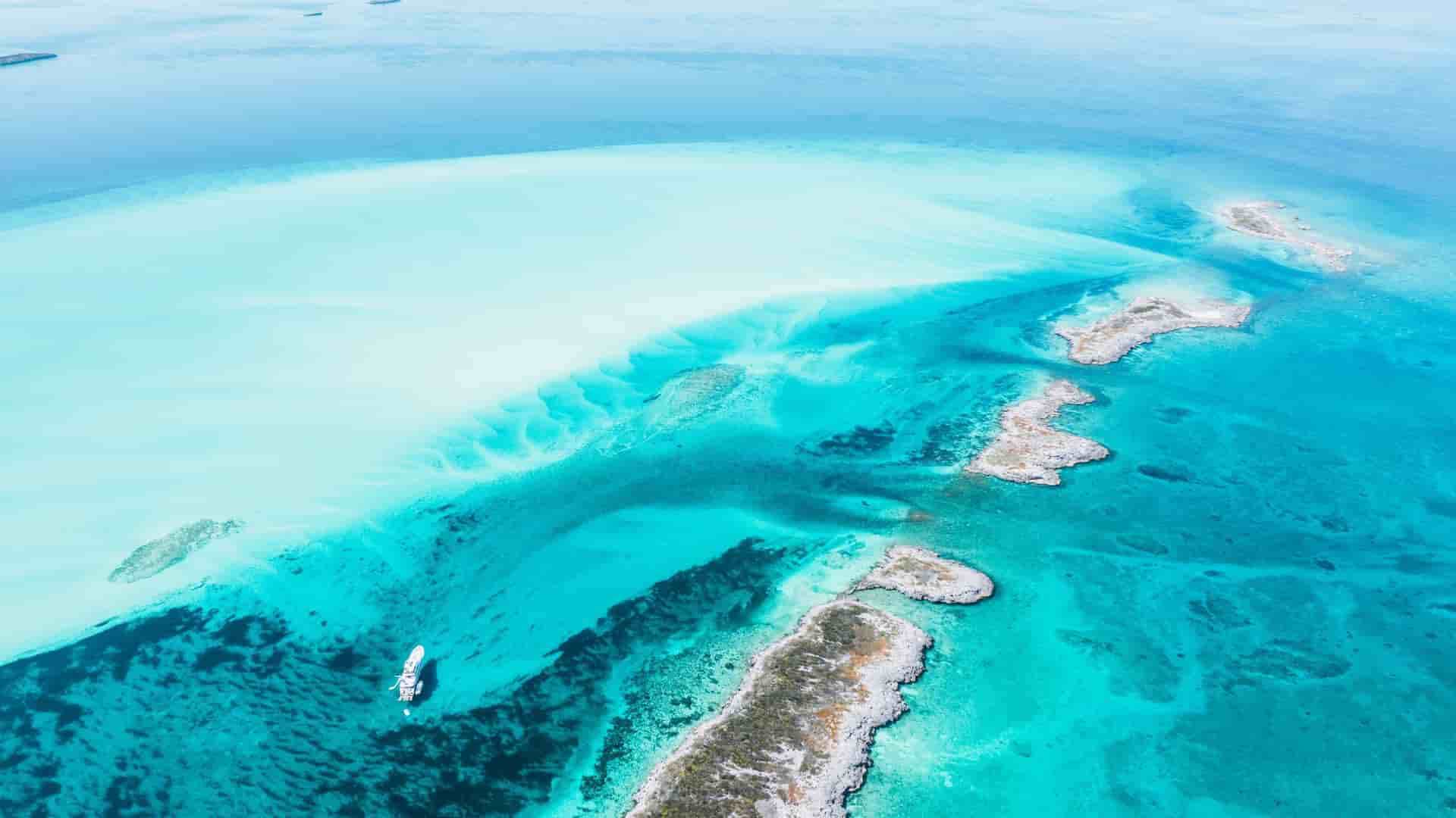 An aerial view of the Old Bahama Channel, showing a small white boat sailing on the stunning turquoise waters and small rocky islands of the Caribbean.