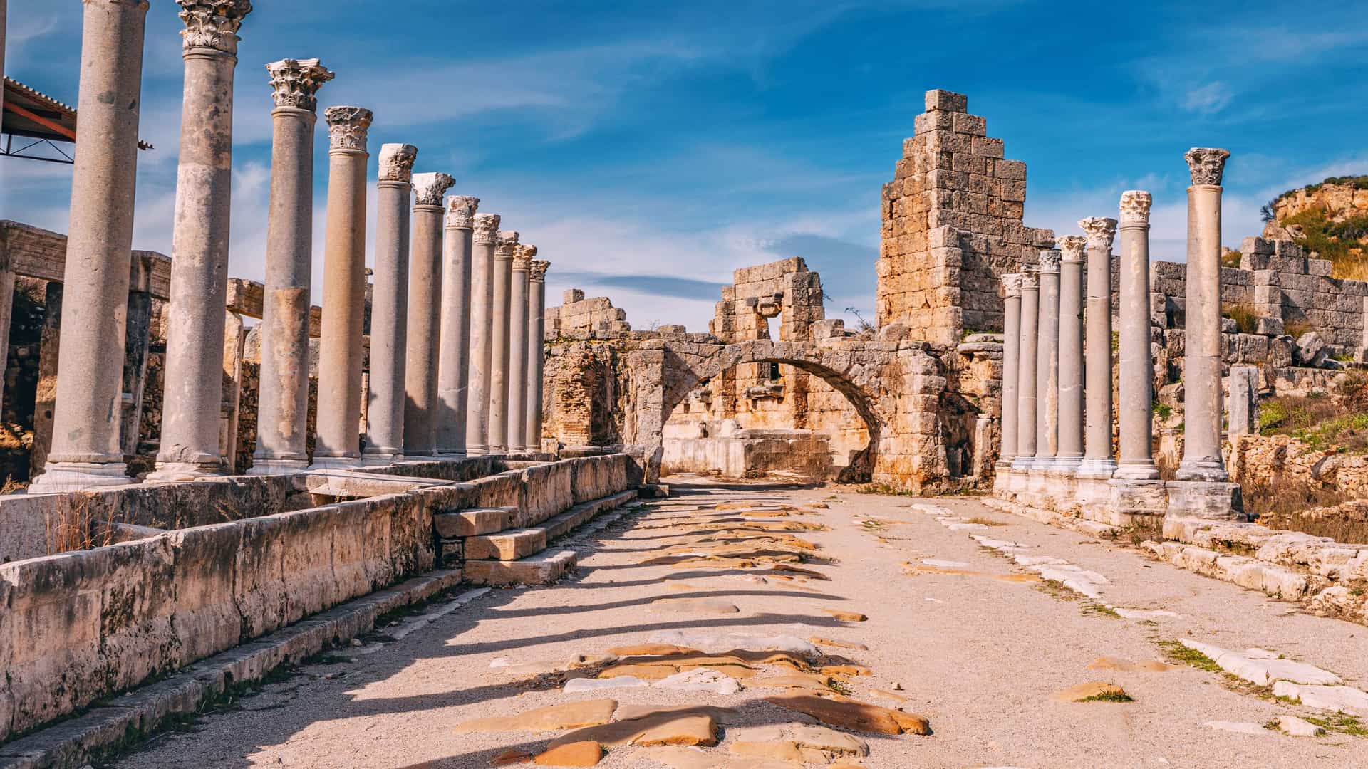 "A scenic shot of the ancient ruins of the Temple of Olympian Zeus in Olympia, Greece, showing a row of massive stone columns under a bright blue sky. "