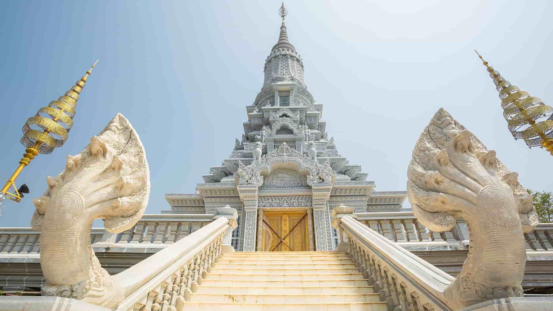 A detailed view of a Buddhist stupa with a white pagoda and two mythical stone serpent statues, a historical landmark at Oudong Mountain, Cambodia.