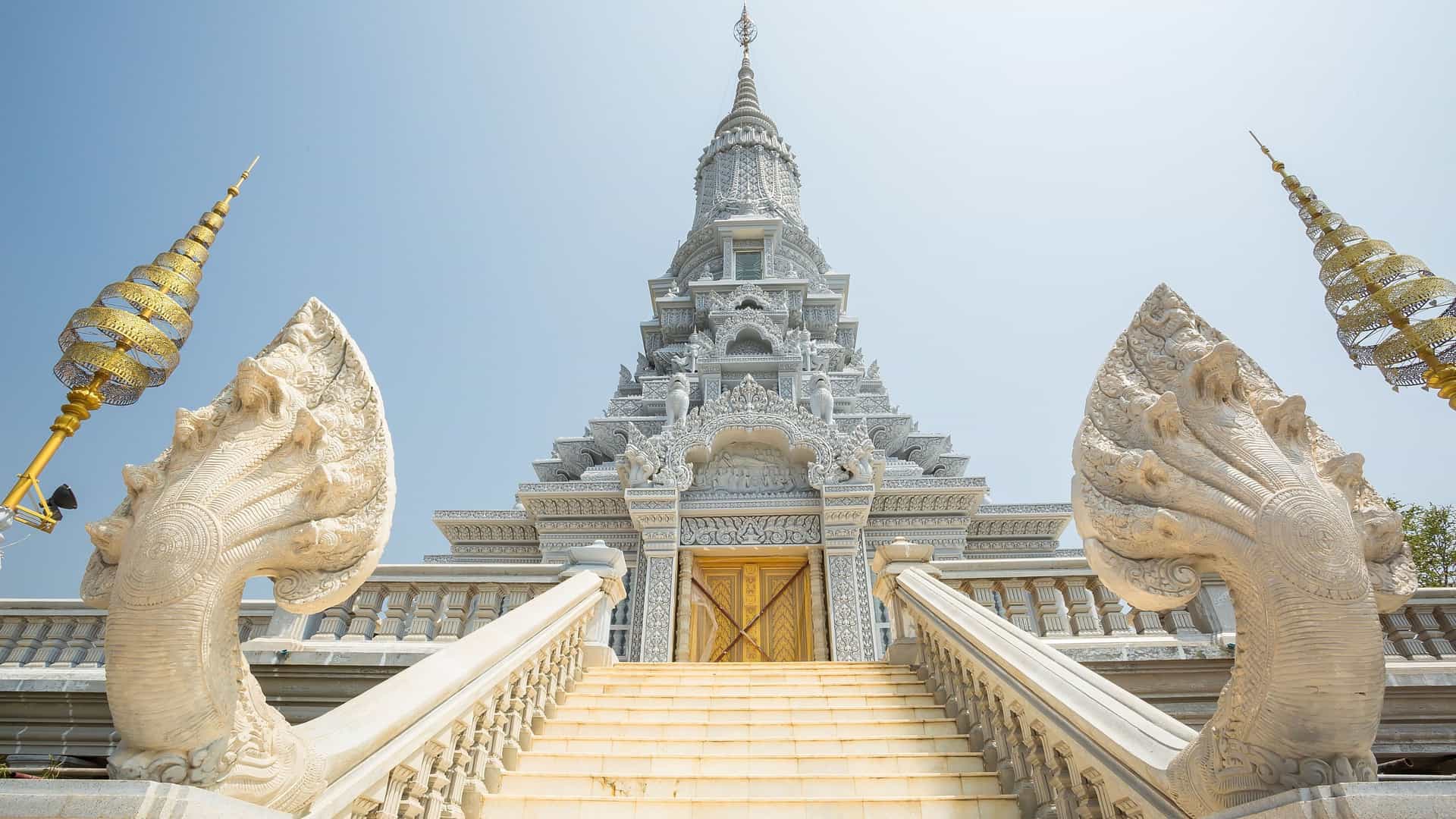 A detailed view of a Buddhist stupa with a white pagoda and two mythical stone serpent statues, a historical landmark at Oudong Mountain, Cambodia.