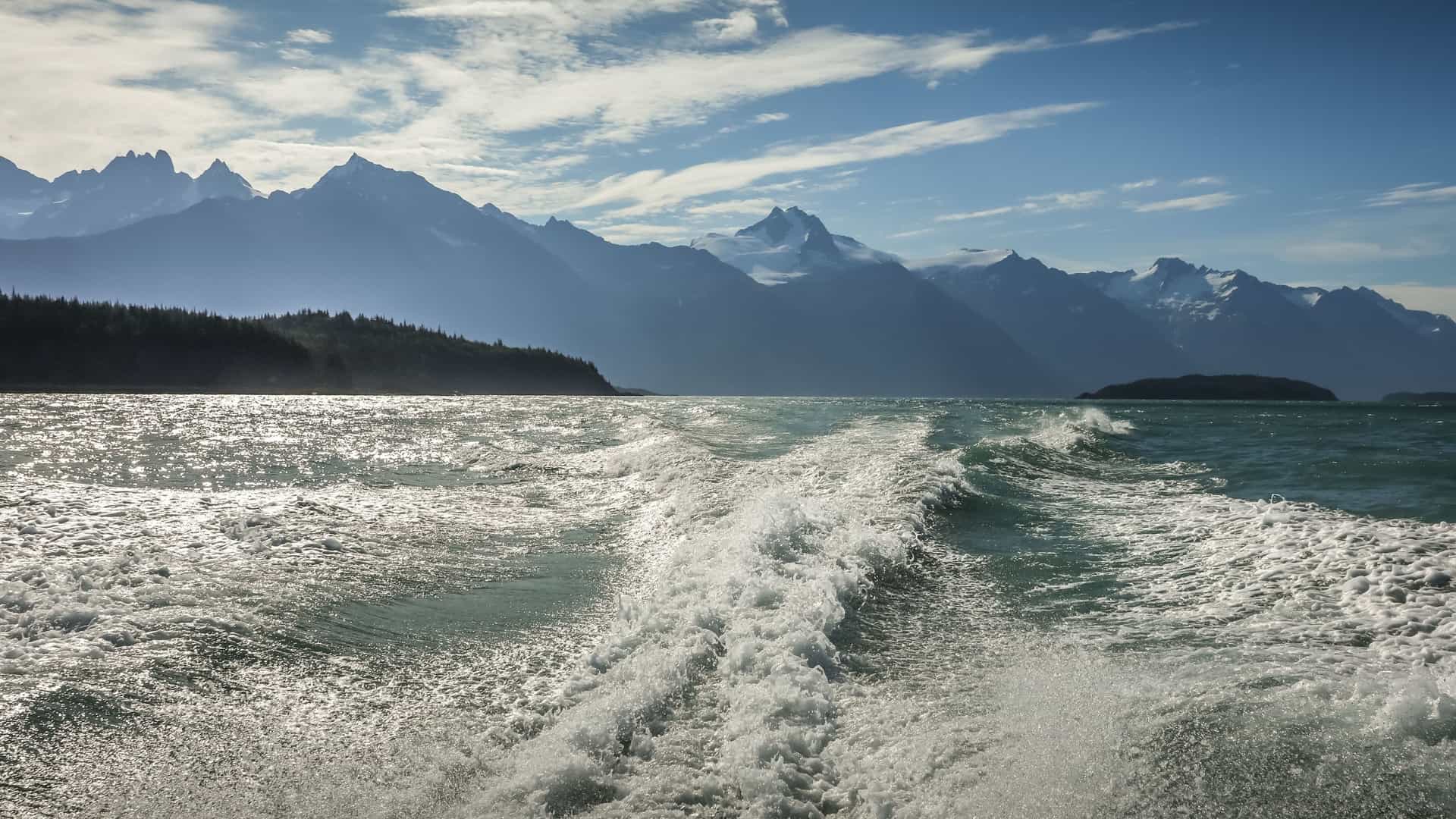 A beautiful view of the Outside Passage in Alaska, with mountains in the background and a boat's wake on the water in the foreground.