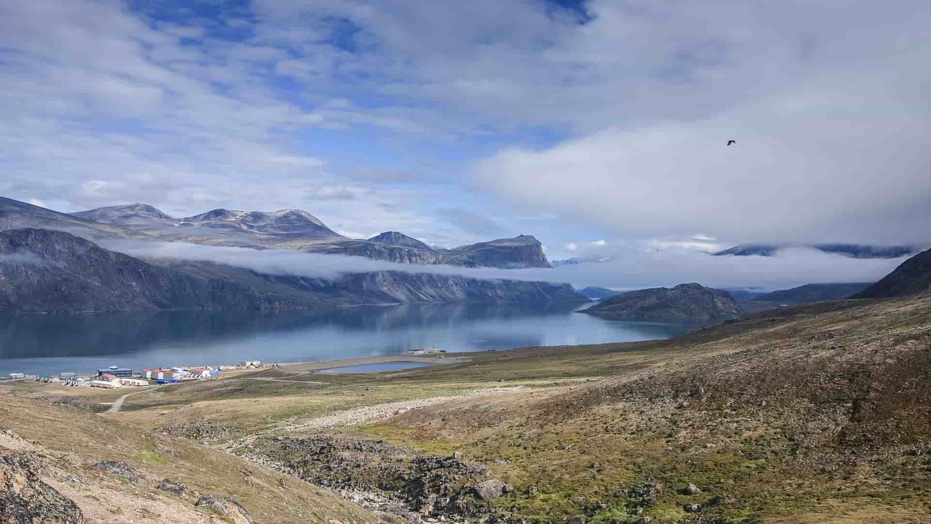 A beautiful scenic shot of the fjord in Pangnirtung, Nunavut, with small buildings along the shore, a huge lake, and clouds obscuring the tops of the mountain peaks.