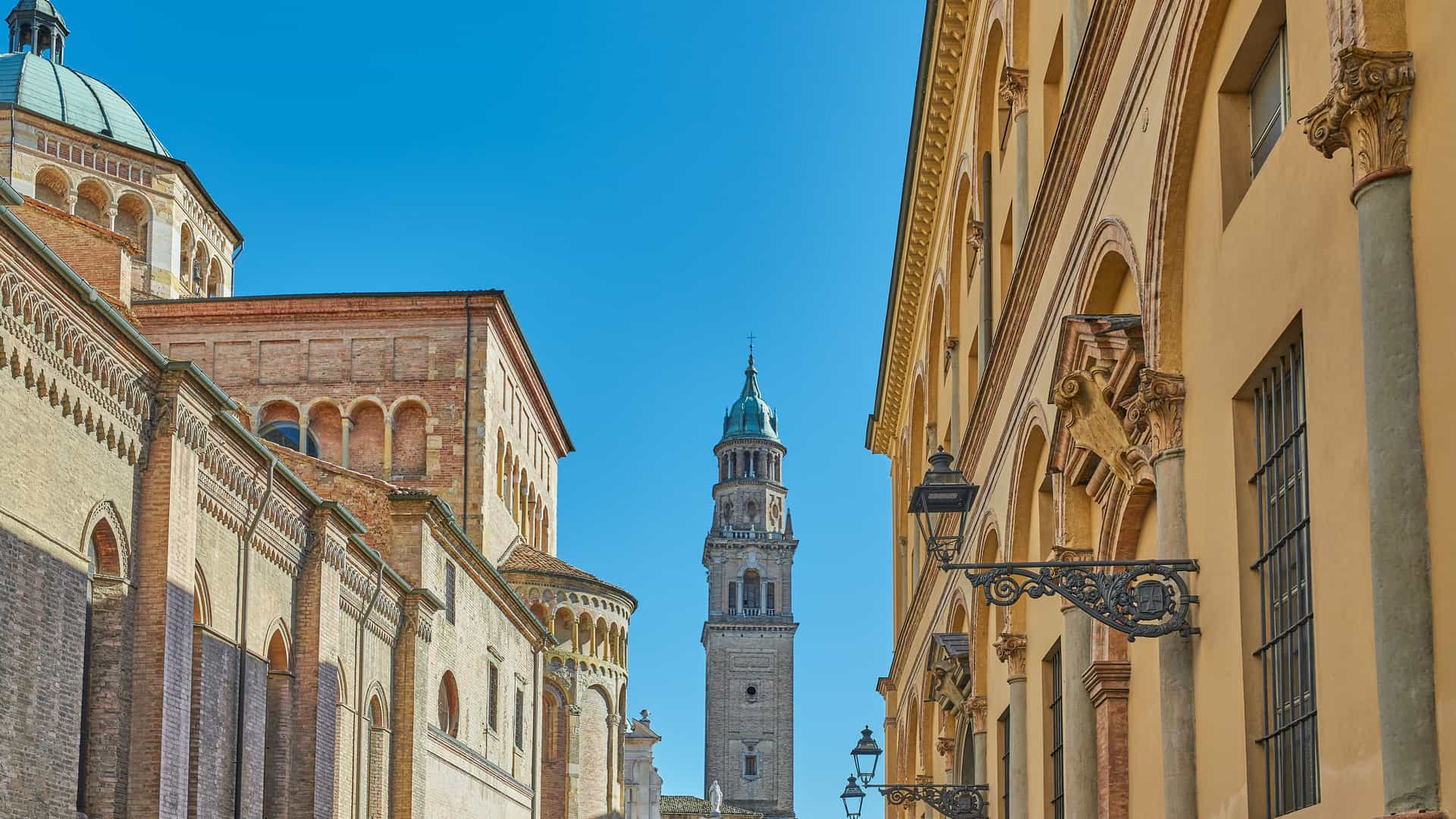 "A stunning low-angle shot of the historic Parma Cathedral and its towering bell tower, the Campanile, visible between two old buildings in Parma, Italy. "