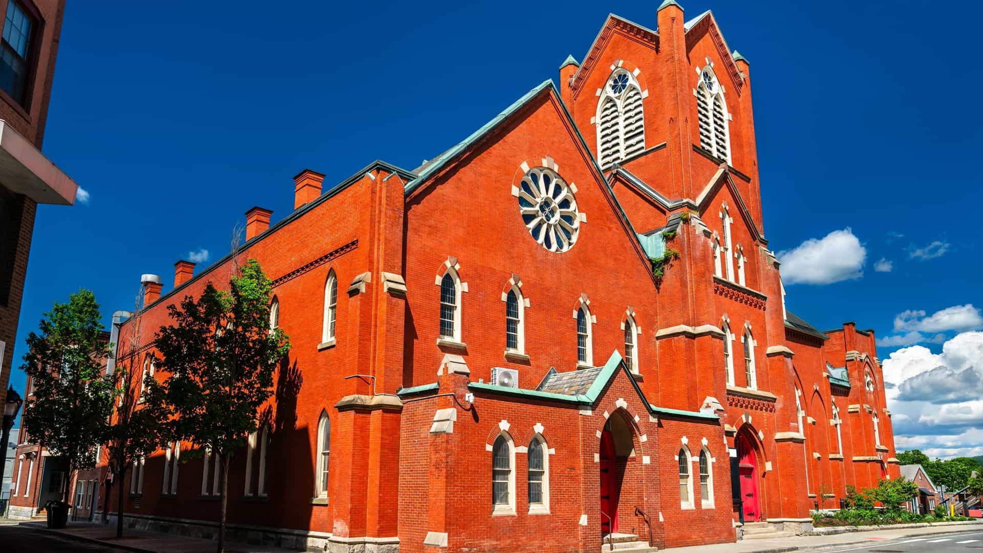 A grand, Gothic Revival style church in Pittsfield, Massachusetts, with a large circular window is constructed entirely of bright red brick.