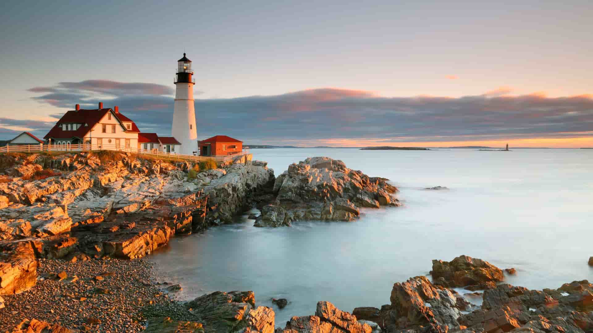 A breathtaking sunrise view of the historic Portland Head Light lighthouse, a famous landmark in Portland, Maine, with the light reflecting off the rugged, rocky coastline and the tranquil Atlantic Ocean.