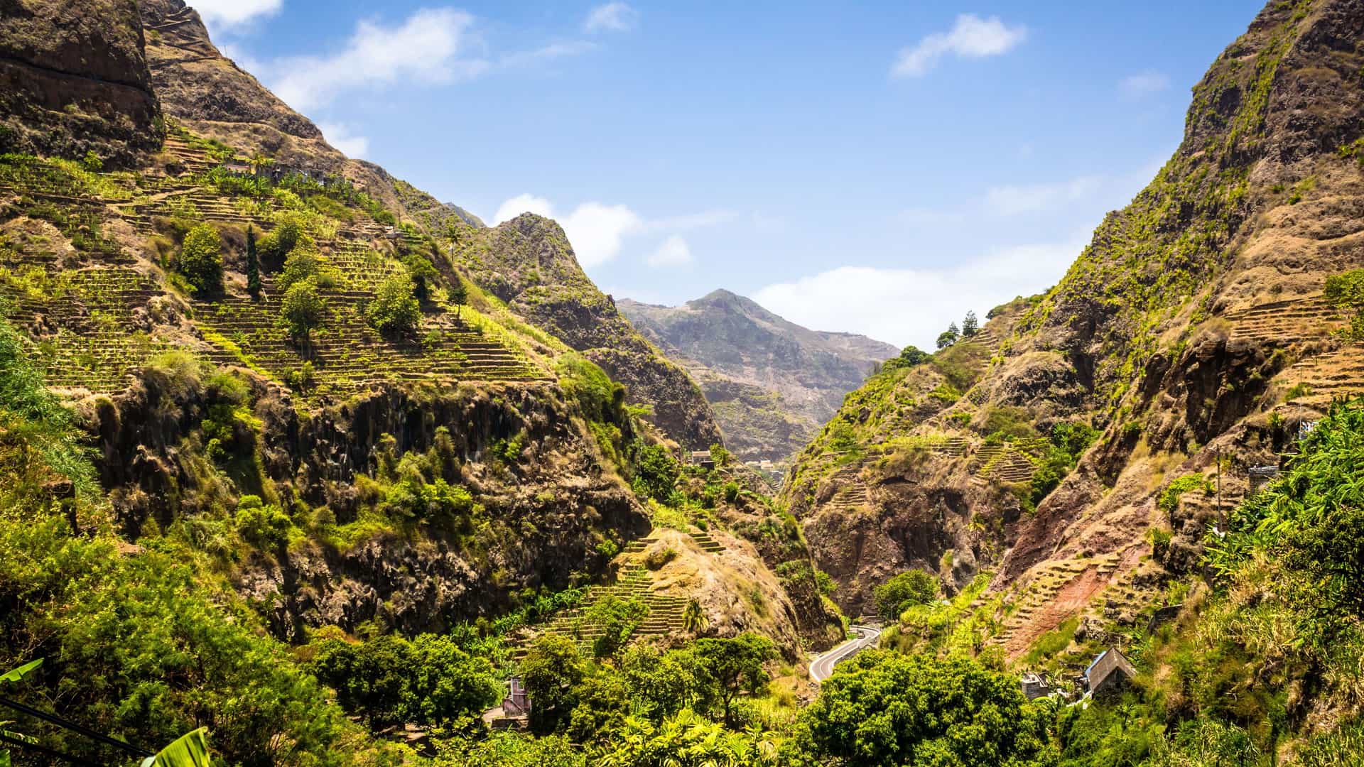 A beautiful panoramic shot of a deep, lush green valley in Praia, Cape Verde, with terraced hillsides and a winding road snaking through the mountainous landscape.
