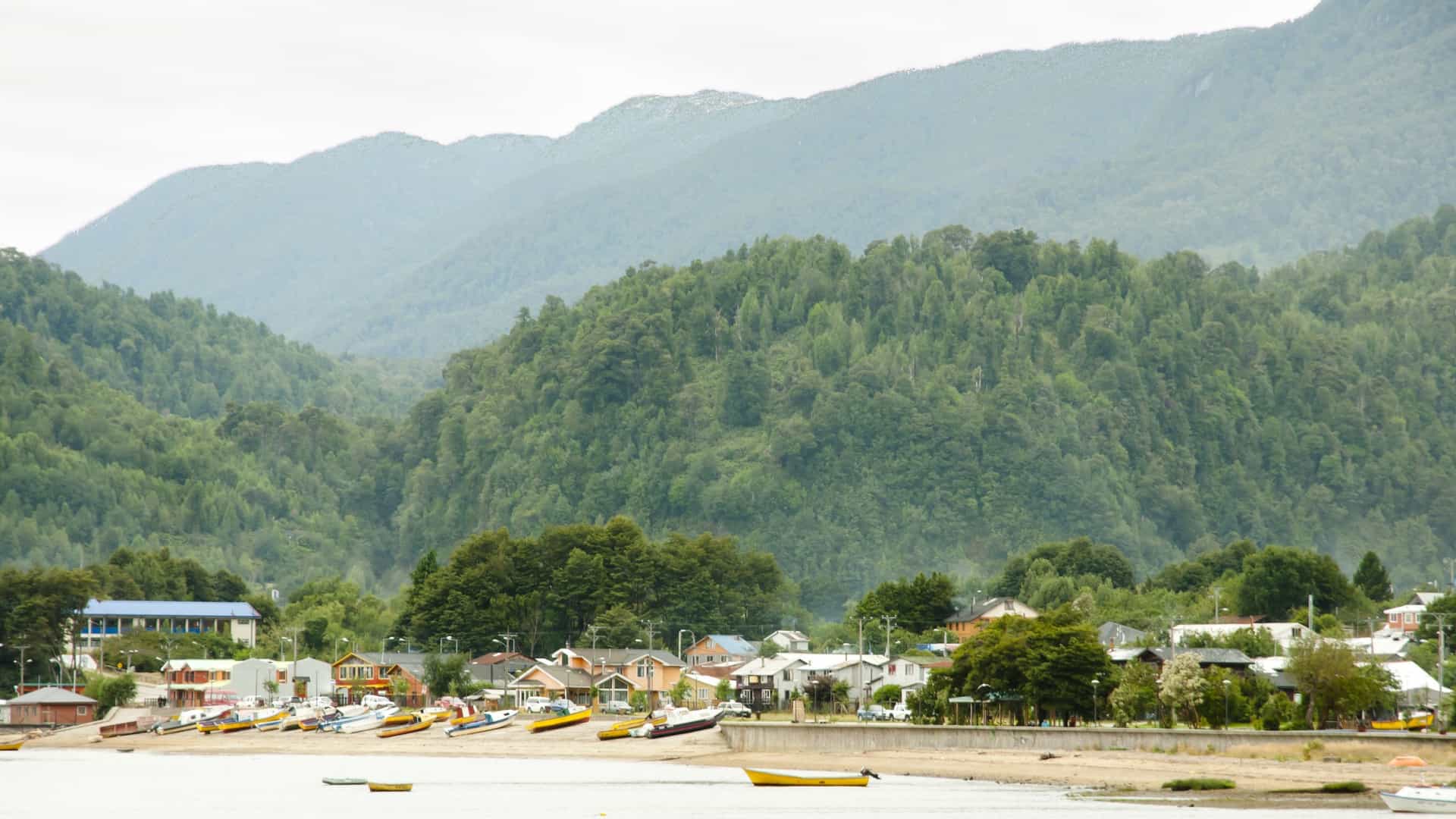 The seaside village of Puerto Cisnes, Chile, nestled against densely forested mountains with small boats lining the shore.