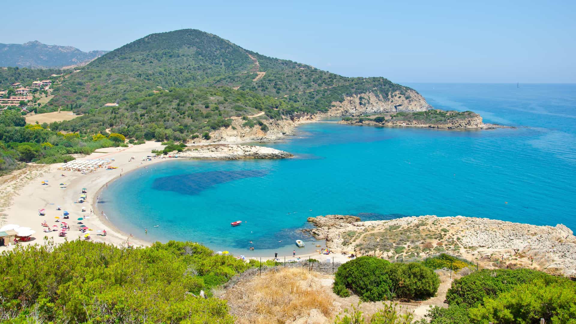 A high-angle view of a stunning crescent-shaped bay with a pristine sandy beach in Pula, Sardinia, Italy, showcasing the calm turquoise waters of the Mediterranean Sea.