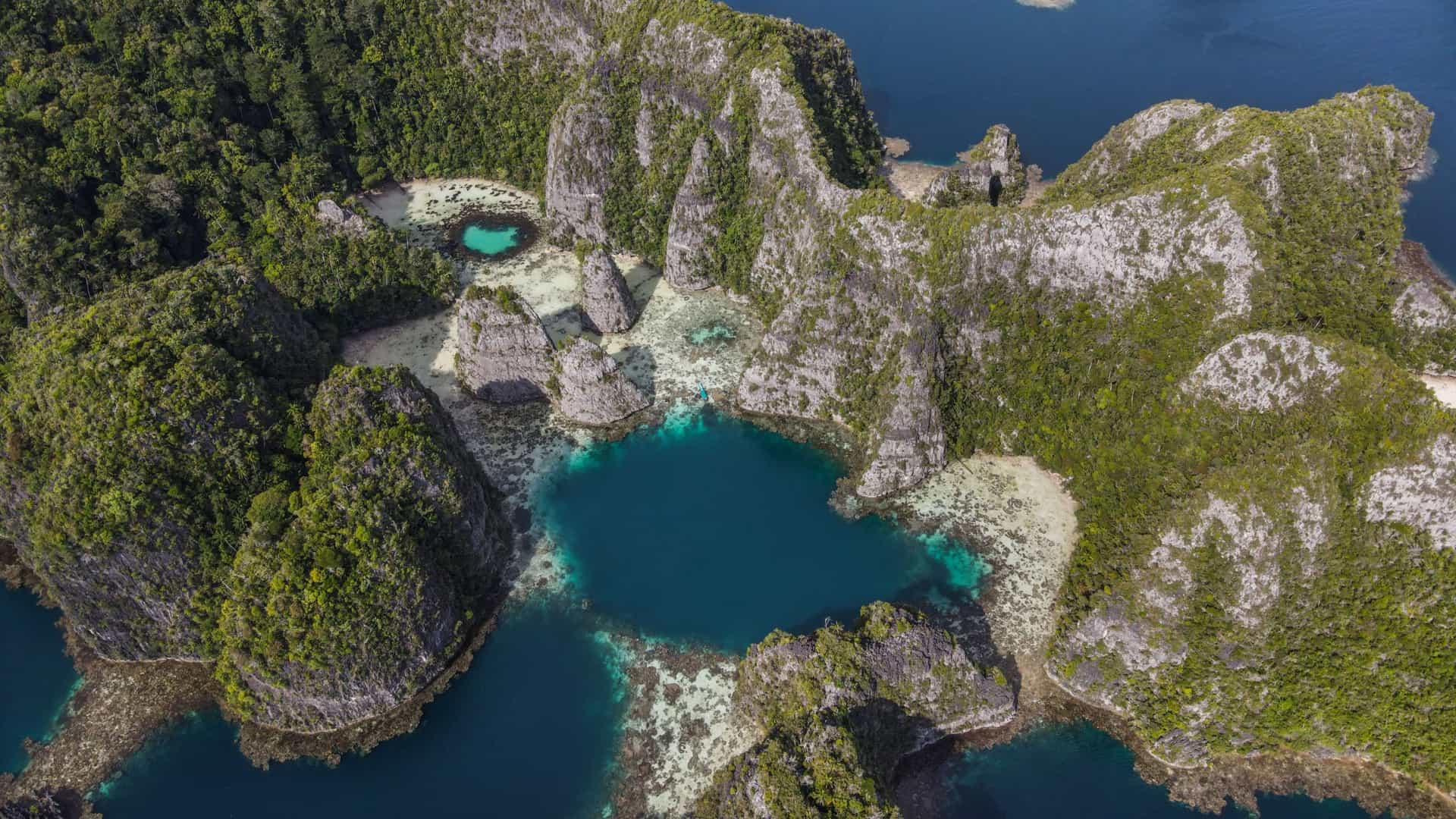 An aerial shot of the stunning natural beauty of Pulau Balbulol, Raja Ampat, showcasing limestone karst islands covered in lush vegetation surrounding a secluded, turquoise-colored lagoon.