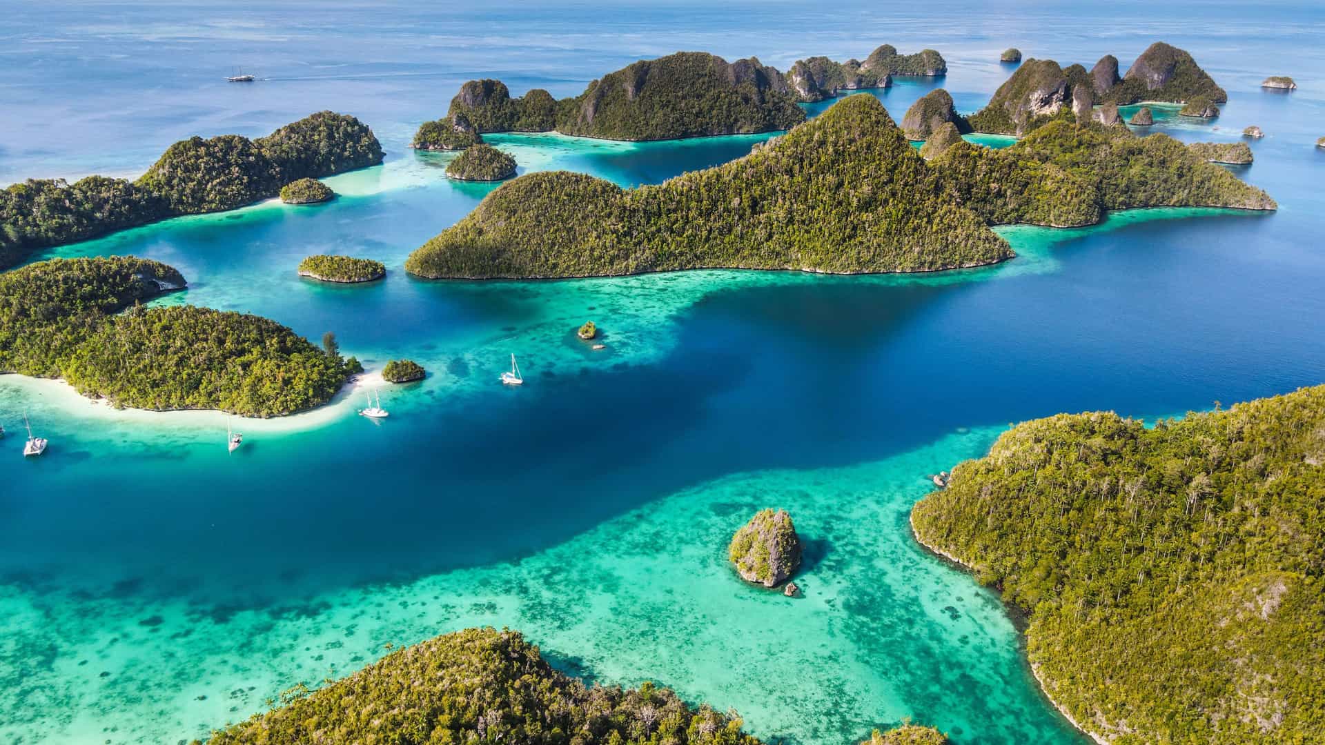 An aerial view of the breathtaking tropical islands of Pulau Num, Raja Ampat, Indonesia, showcasing stunning limestone karst formations covered in green foliage surrounded by crystal-clear turquoise waters and coral reefs.