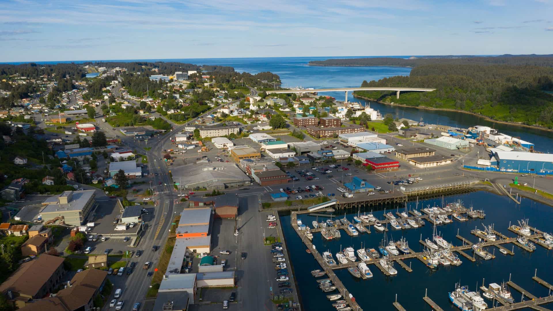 An aerial shot of the town of Ramah Bay, Labrador, with a marina full of fishing boats and a bridge leading to a landmass on a sunny day.