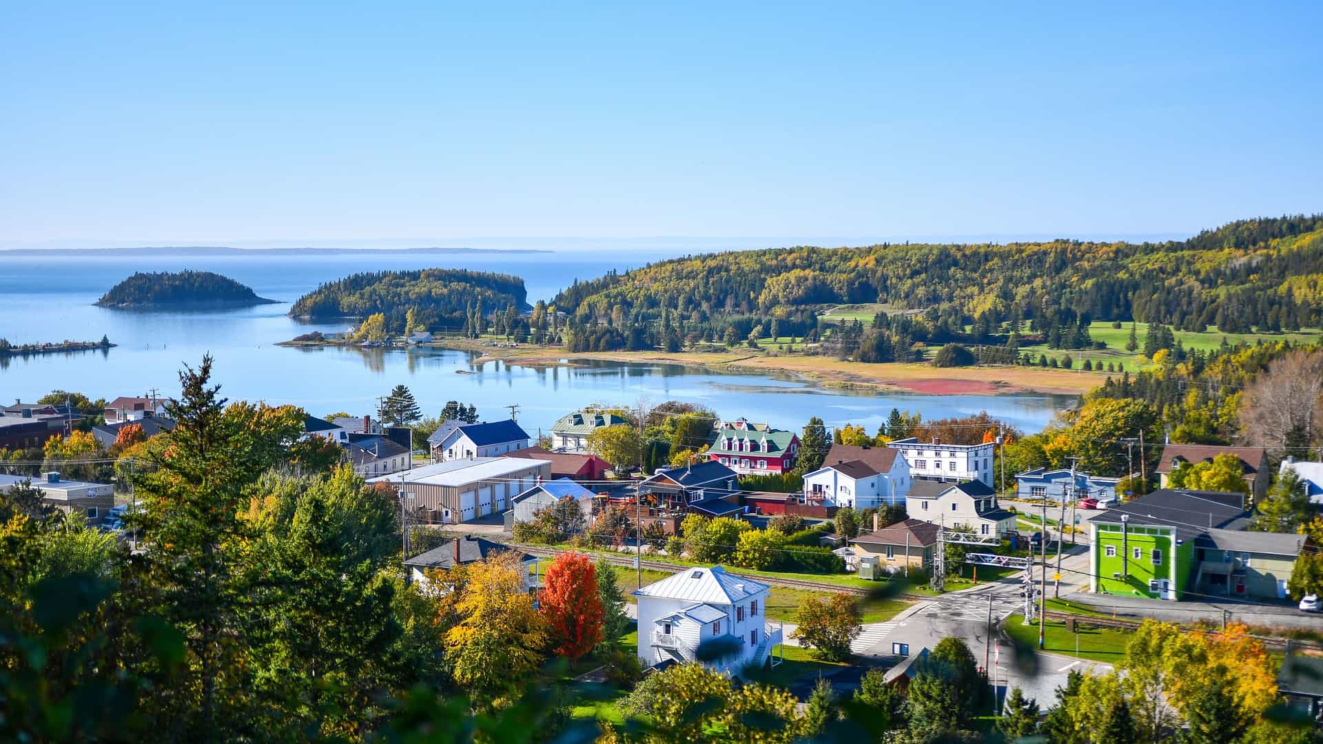 "A picturesque village on the water's edge in Rimouski, Canada, with colorful houses surrounded by lush green forests in the beautiful Bas-Saint-Laurent region. "