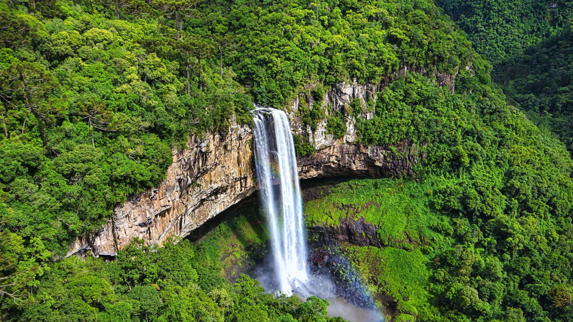 A scenic view of a majestic waterfall cascading down a sheer cliff face into a lush green forest in the Rio Grande region of Brazil.