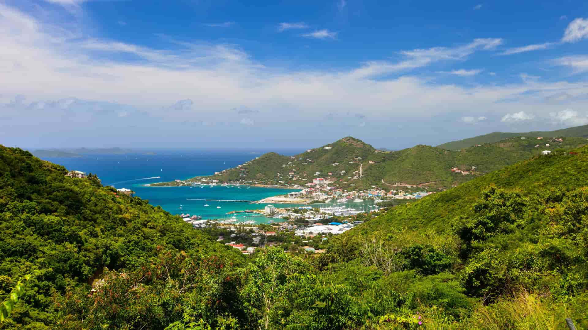A stunning panoramic view of Road Town on Tortola, British Virgin Islands, showing the harbor filled with boats and a small town surrounded by lush green hills overlooking the Caribbean Sea.