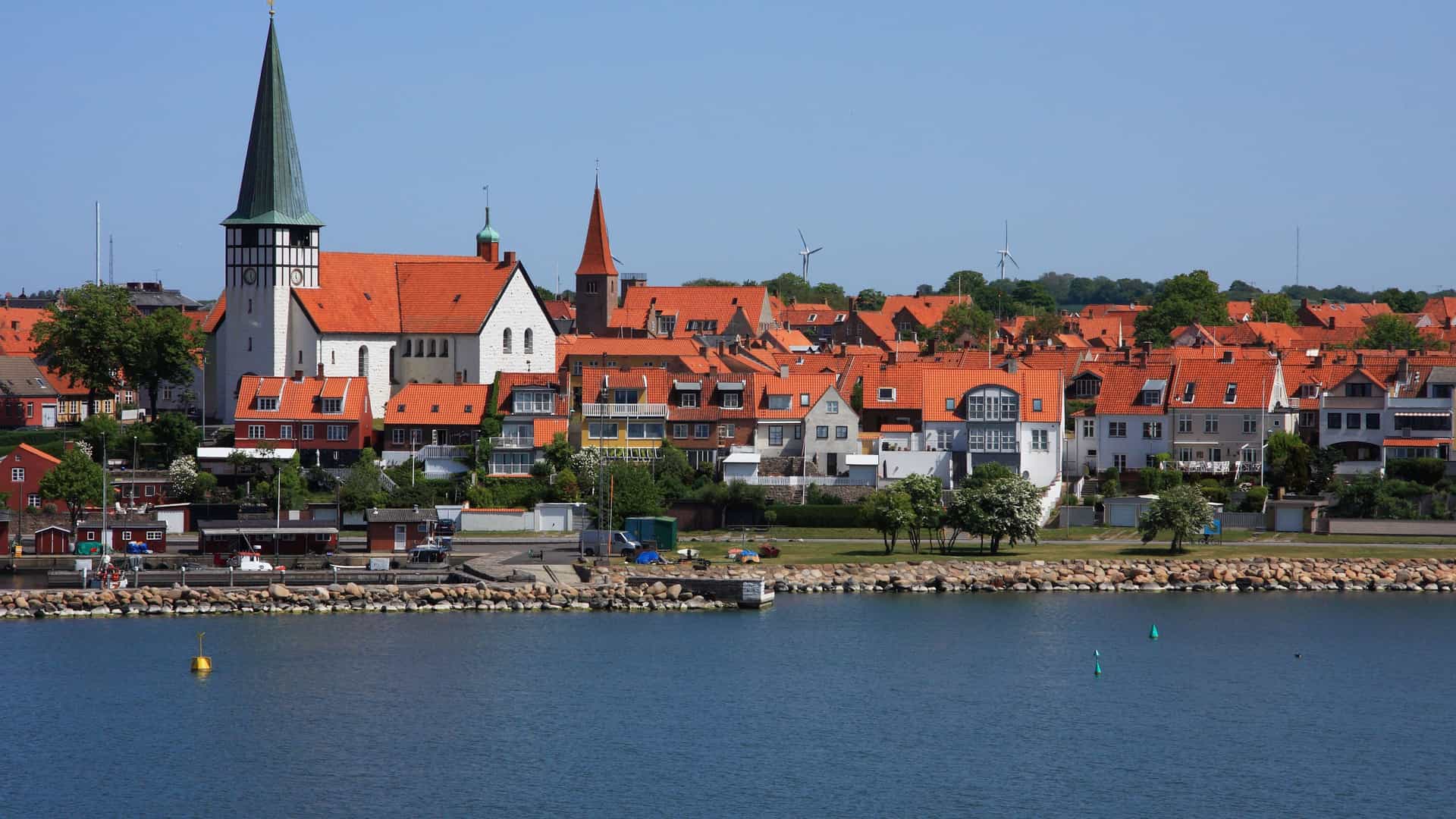 A beautiful view of the coastal town of Rønne, Denmark, featuring the iconic St. Nicolai Church and a skyline of red-roofed buildings along the waterfront.