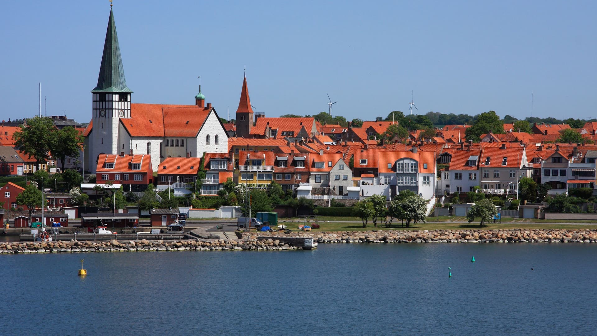 A beautiful view of the coastal town of Rønne, Denmark, featuring the iconic St. Nicolai Church and a skyline of red-roofed buildings along the waterfront.