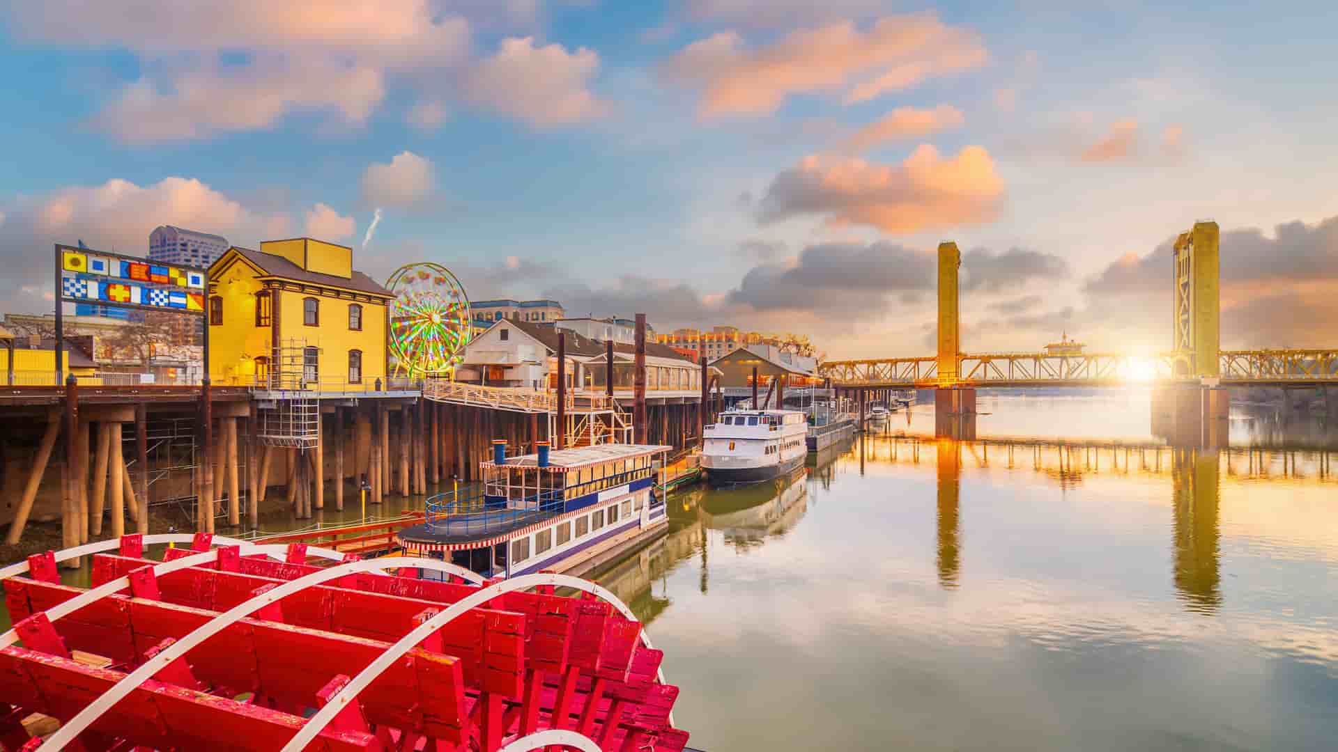 "A picturesque sunset view of Old Sacramento, California, with the iconic Tower Bridge and riverboats on the Sacramento River, a popular tourist destination. "