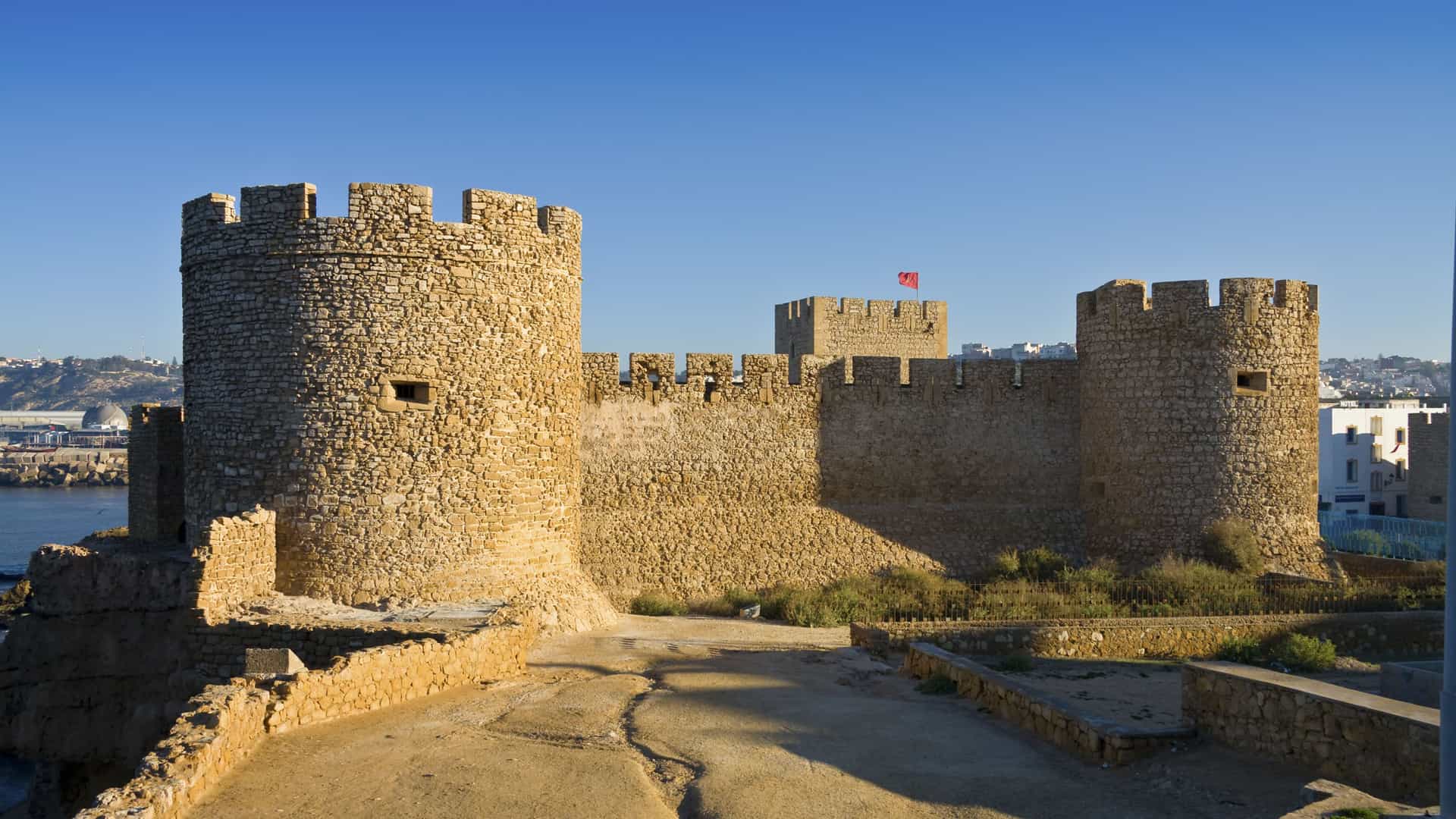 A large, ancient fortress with crenellated walls and towers, known as the Kechla fortress, overlooking the Atlantic Ocean in the coastal city of Safi, Morocco.