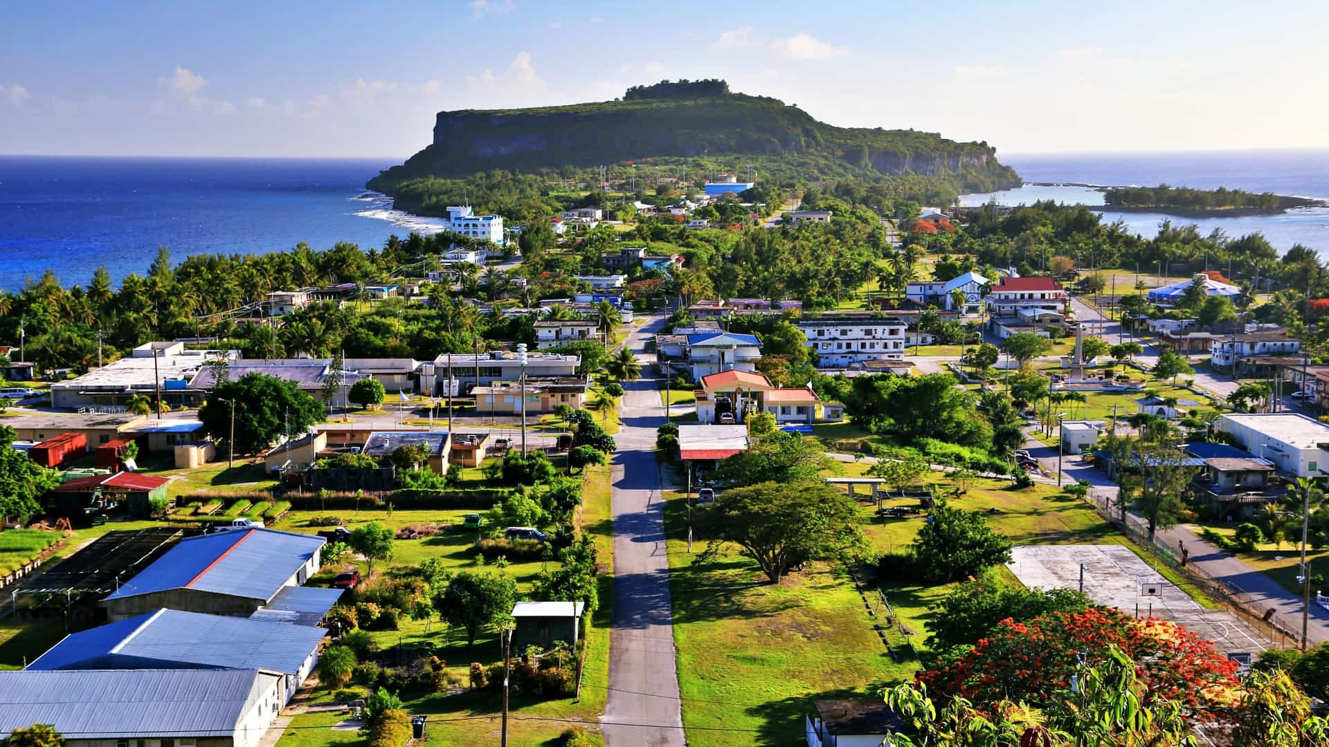 An aerial view of a small residential town with a large, flat-topped cliff overlooking the ocean on Saipan, Northern Mariana Islands.