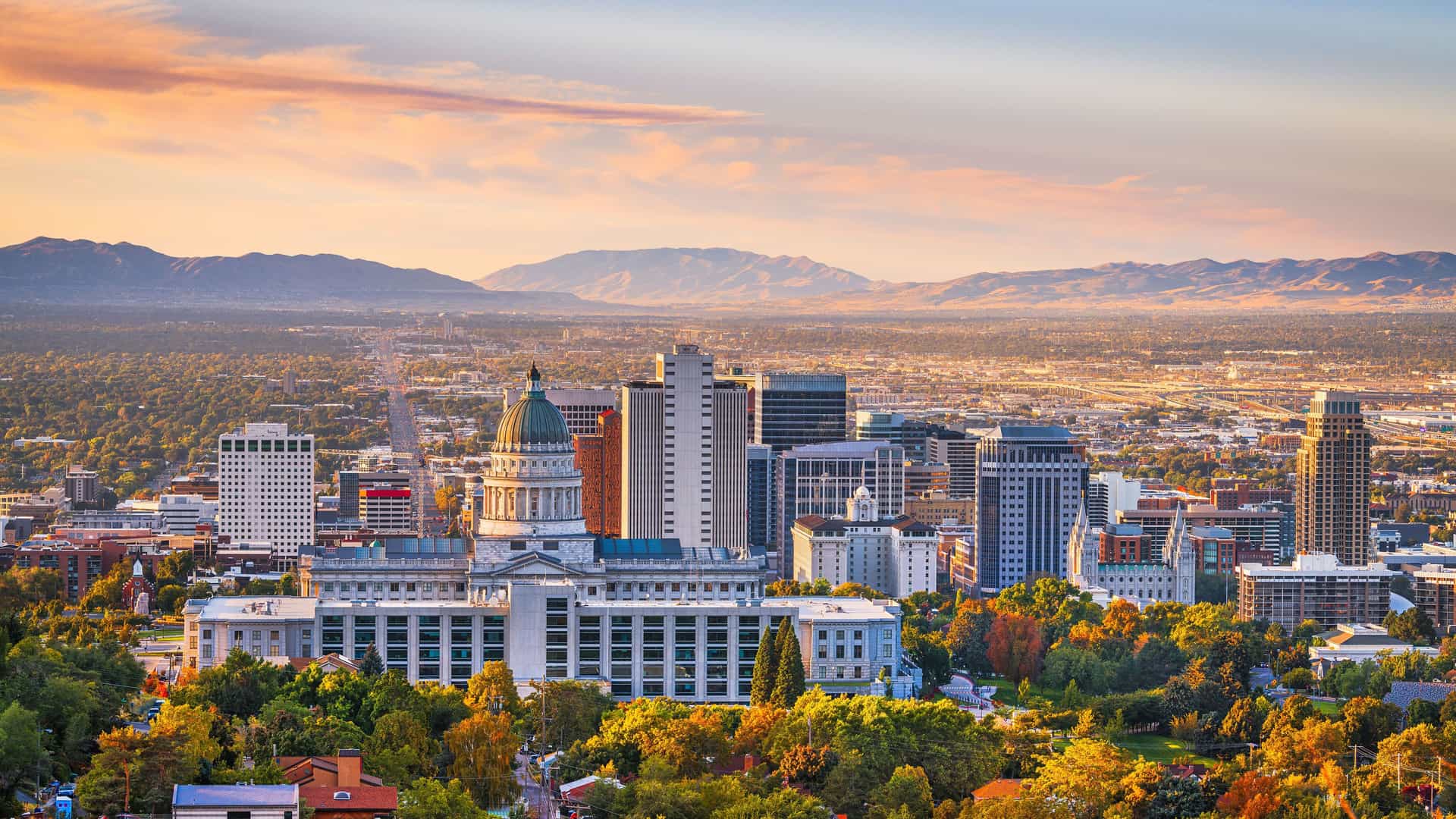 "A stunning sunset panoramic view of downtown Salt Lake City, Utah, with the historic State Capitol building in the foreground, and the dramatic Wasatch Mountains in the distance. "