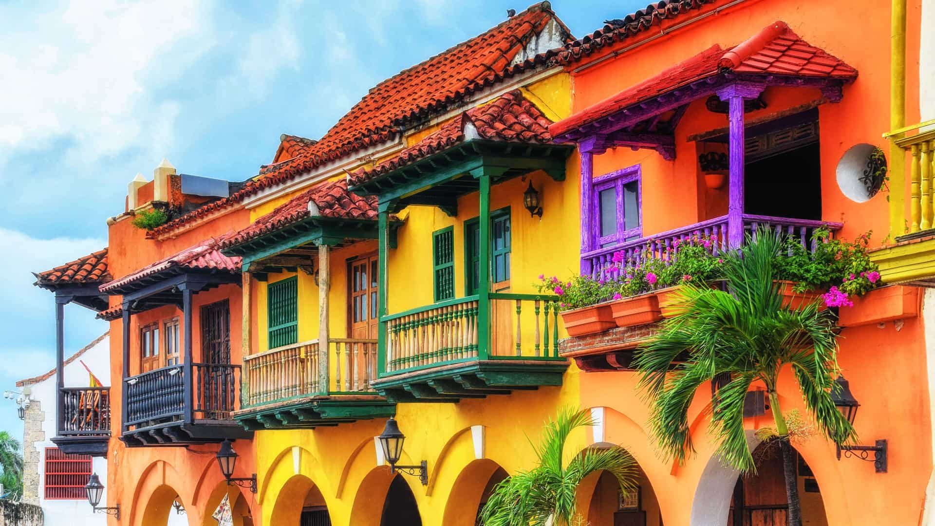 A close-up of a row of colonial buildings with vibrant, colorful facades in San Basilio de Palenque, Colombia, featuring brightly painted balconies and red-tiled rooftops.